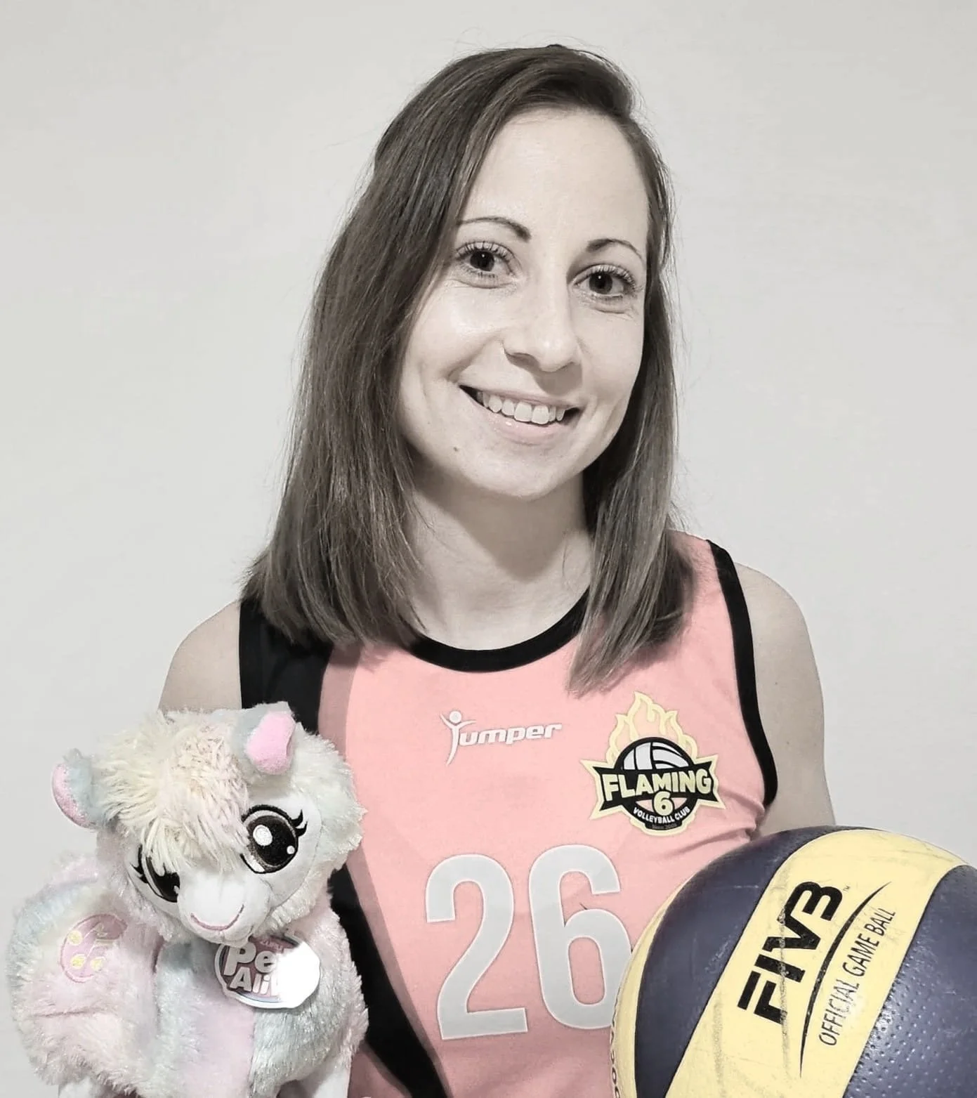A smiling woman in a volleyball uniform holding a volleyball and a plush toy llama.