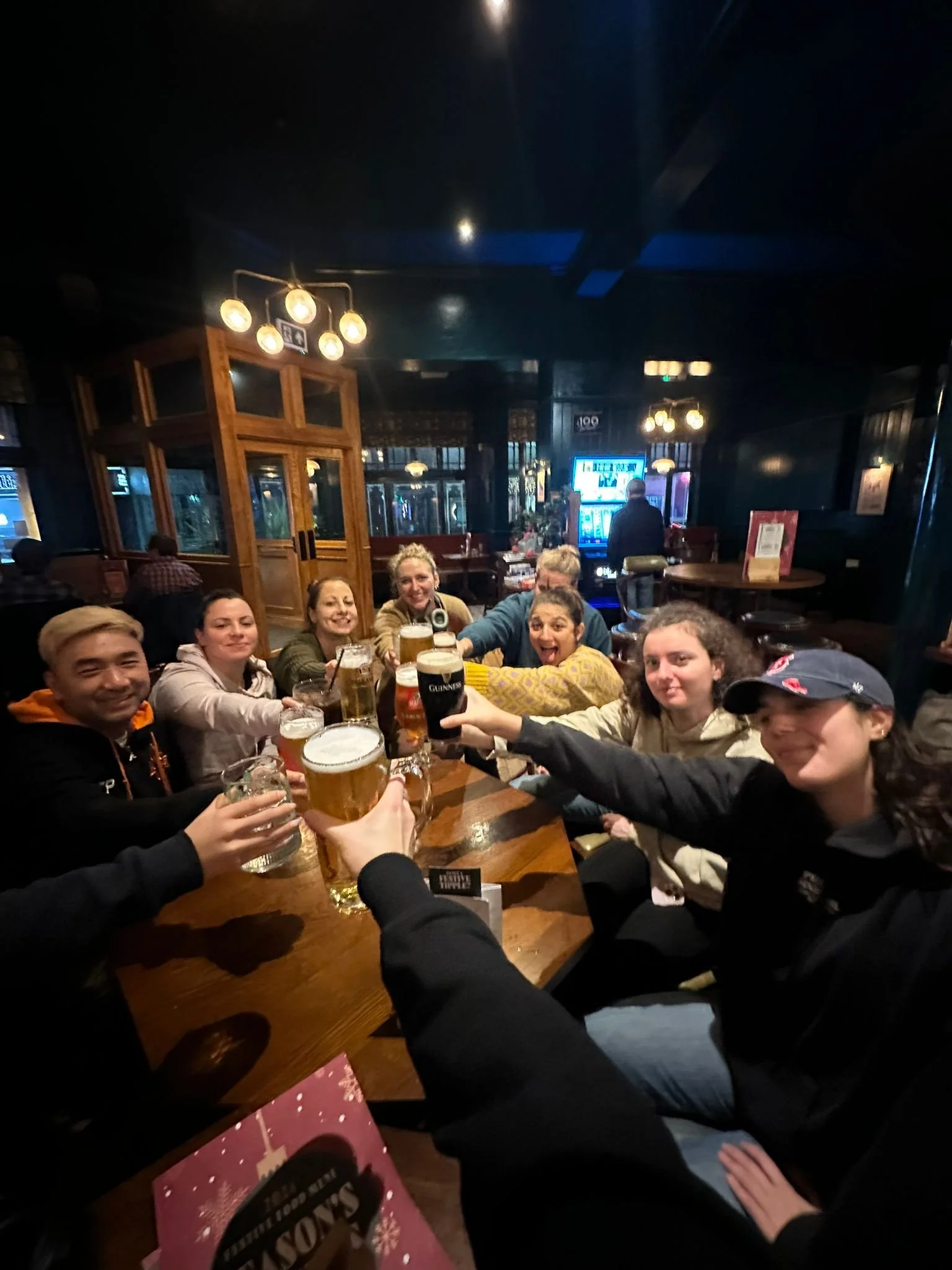 Group of friends gathered around a table in a pub, raising their glasses of beer for a toast.