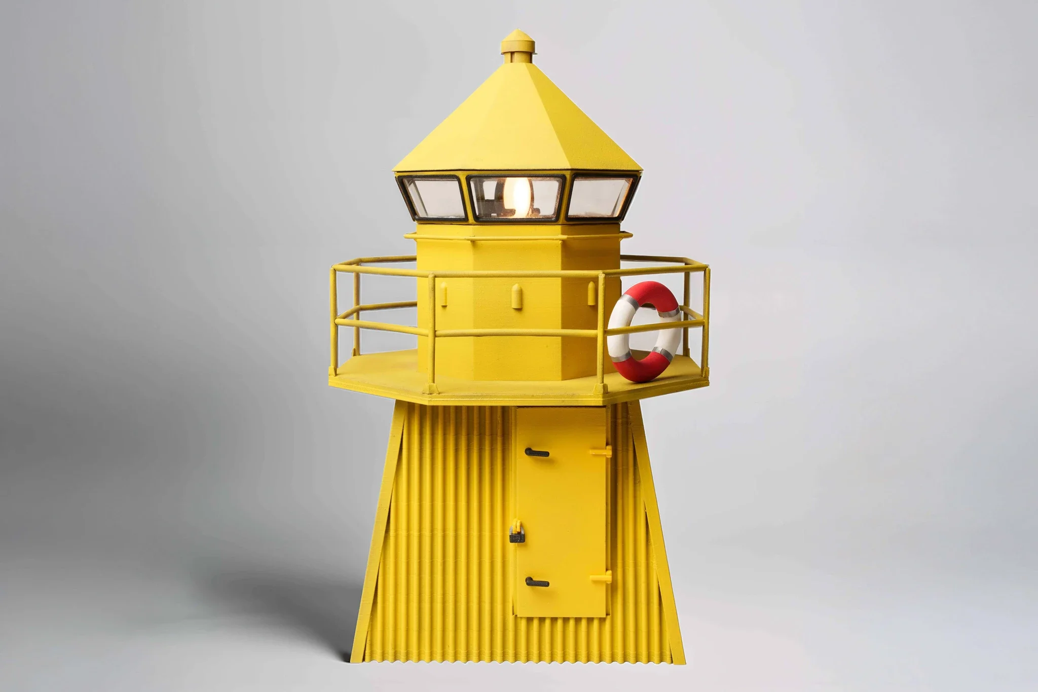 A yellow lighthouse-shaped structure with a gray roof, windows, a red and white life preserver, and a door.