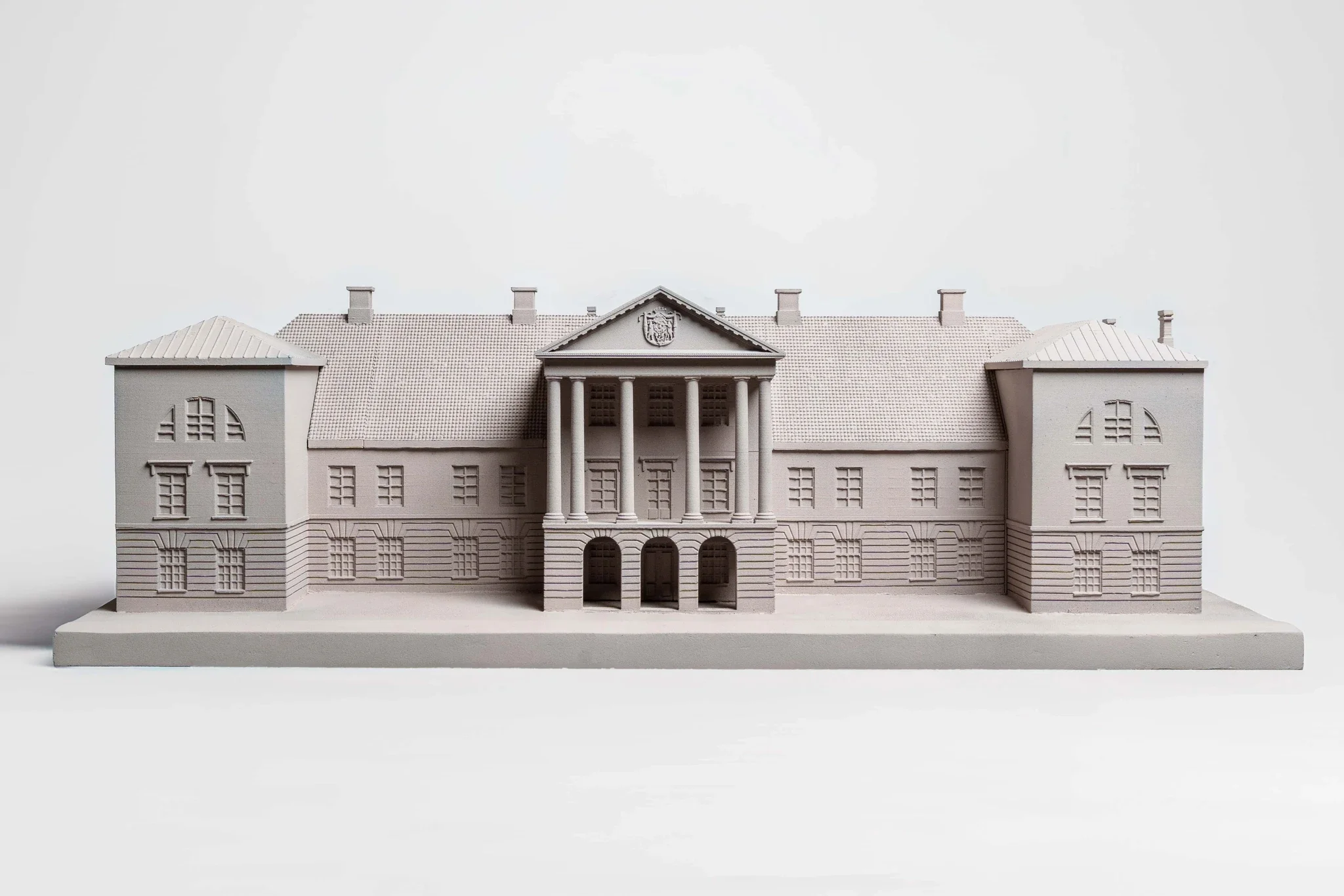 A detailed gray architectural model of a large, historic building with a central portico supported by columns, symmetrical windows, and decorative elements on a white background.