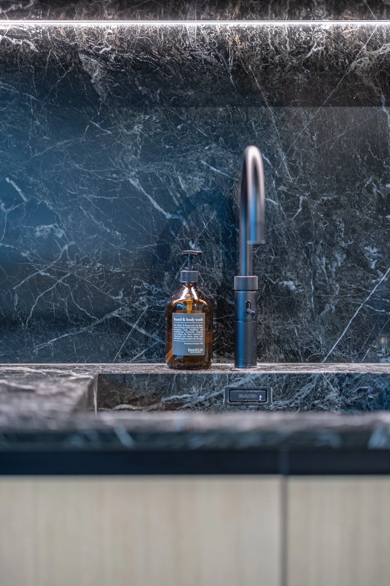 Bathroom sink area with a black marble wall, a modern black faucet, and a brown liquid soap dispenser labeled 'hand & body wash' on the marble countertop.
