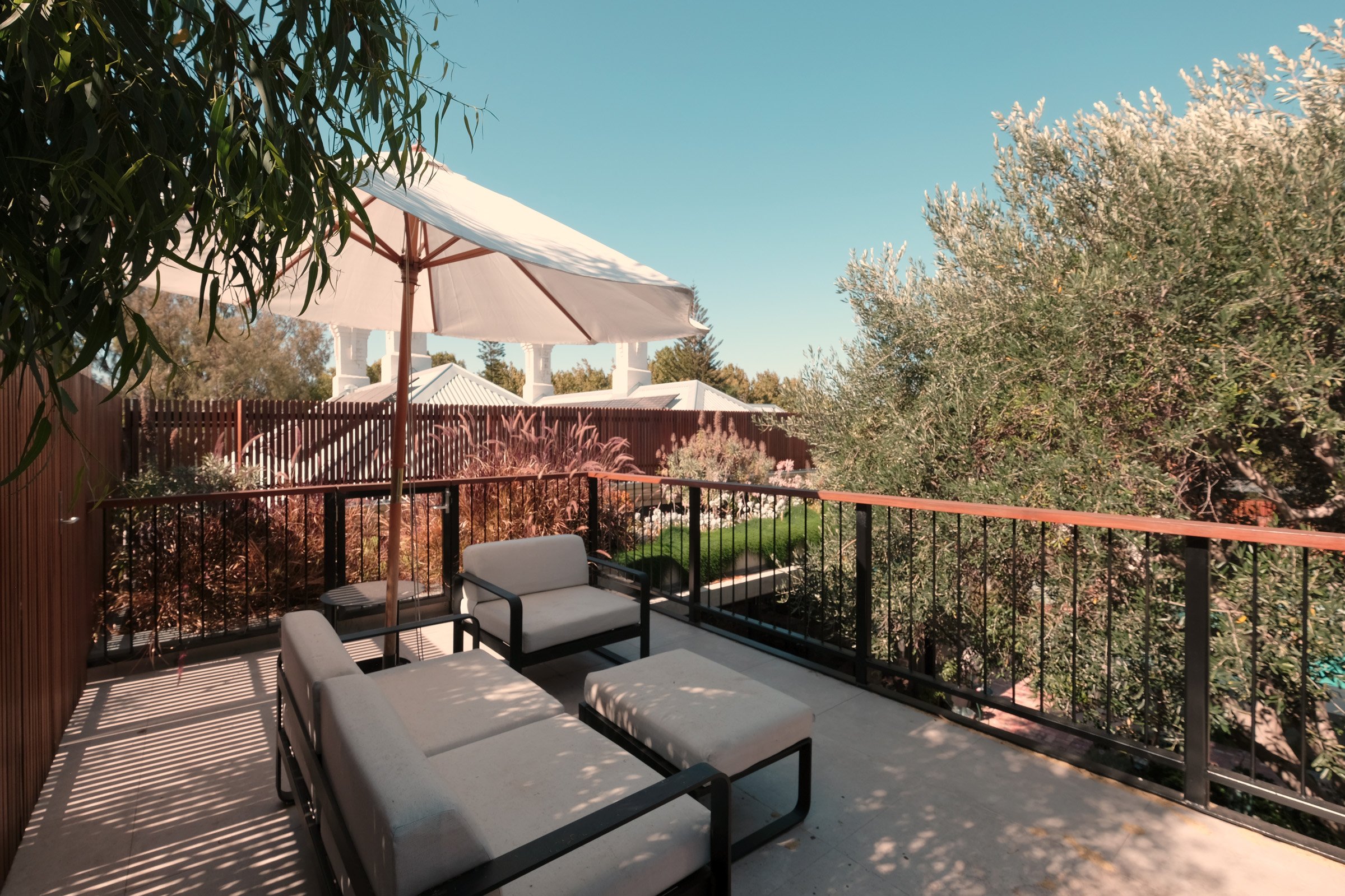 A house with a white exterior, plants, and bicycles under a porch, partially obscured by trees.