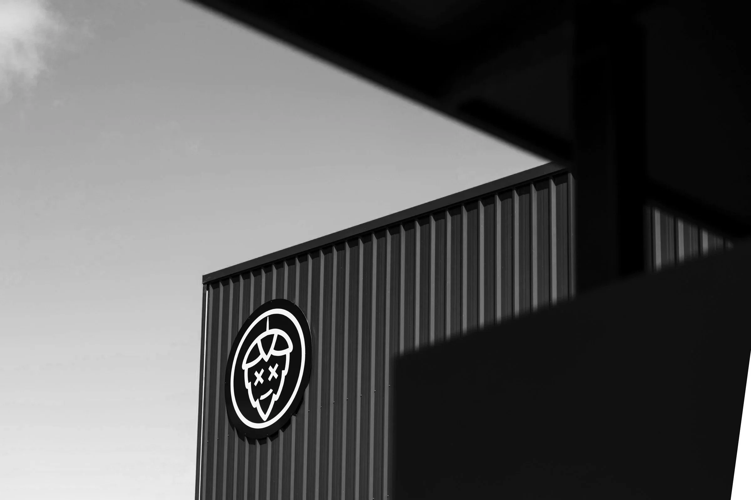 Black and white photo of a building with a stylized skull logo on the front, partially obscured by a dark shadow or structure.