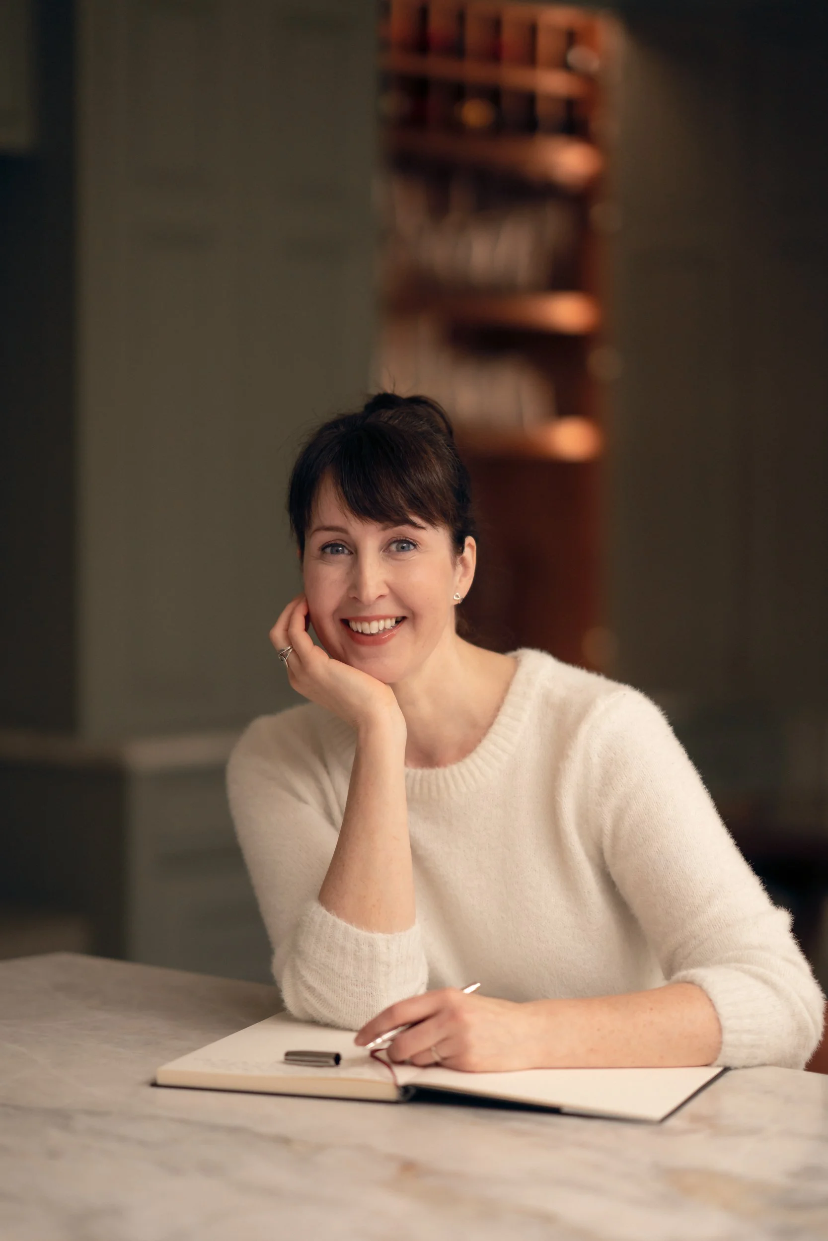 Photo of the author Fiona McCann sitting in a house with a notepad and pen, smiling to camera.