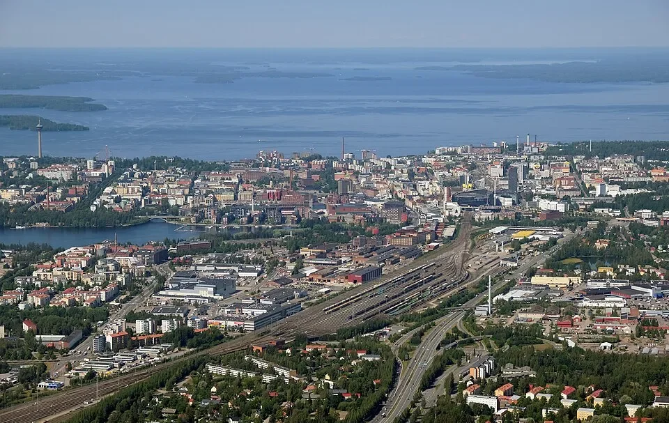 Kaupunkimaisema, korkealta otettu kuva, näkyvissä järvi, rakennuksia, teollisuus- ja liikennealueita, teitä ja rautatiealueita.