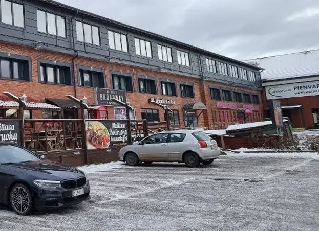 Lähi- ja ravintolaliikealueen rakennus, jossa omistuksessa parkkipaikka ja muutama auto, osa rakennuksesta on punamuurista ja osa puuta, talvinen sää.