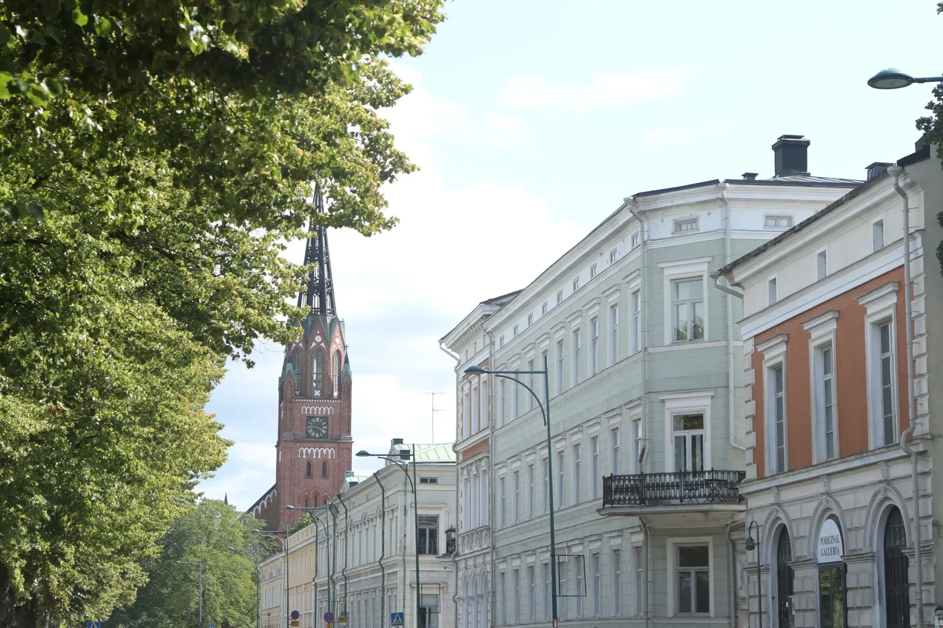 Kuvassa kaupungin katu ja vanhoja rakennuksia, kirkkotorni ja puut liittyvät lisää rakenteisiin, selkeä taivas.