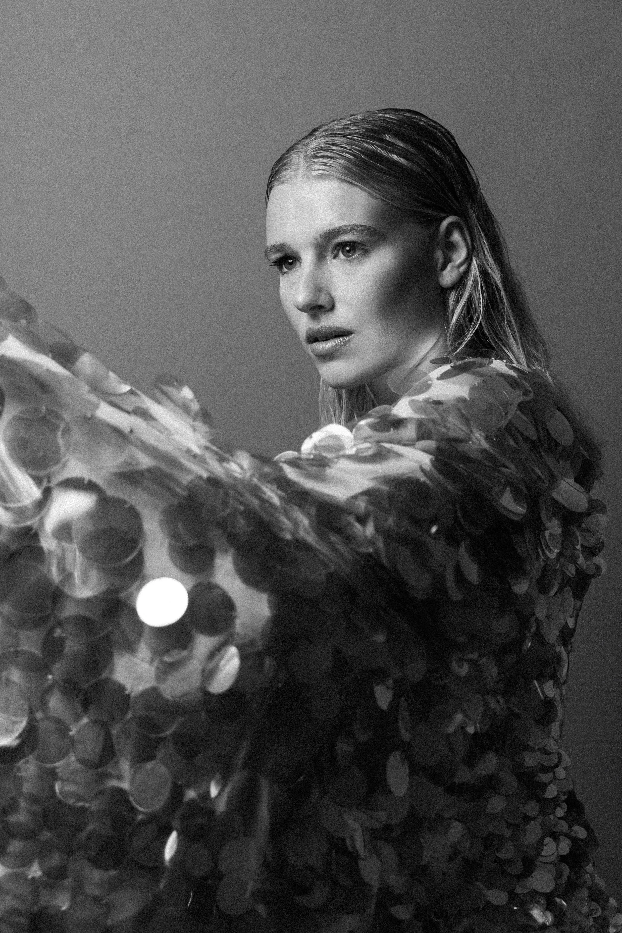 Black and white photo of a woman with wet hair, wearing a sequined jacket, looking to the side.