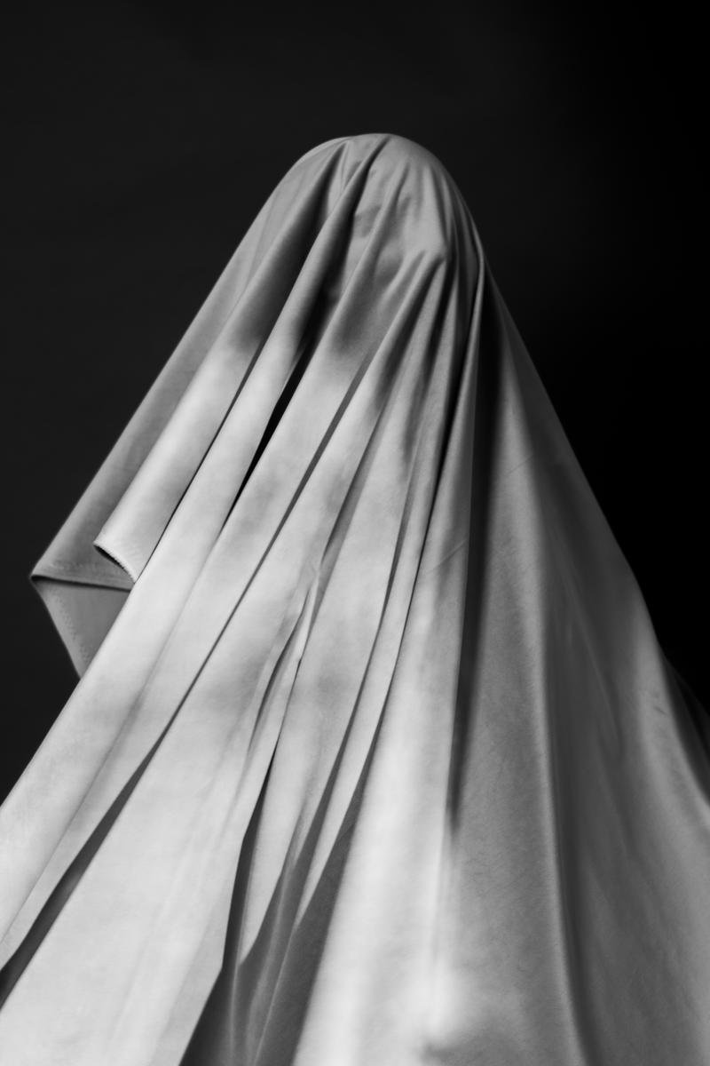 A figure covered with a draped cloth against a dark background.
