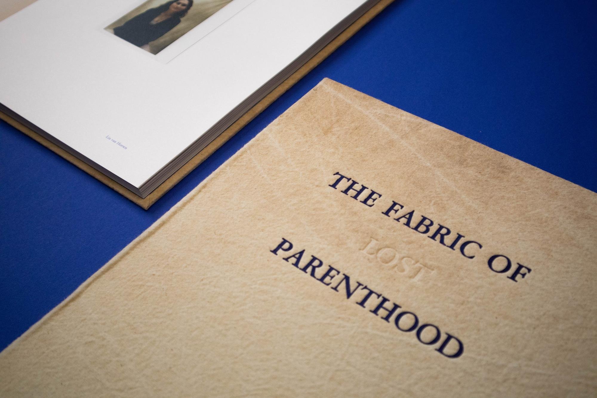 A beige fabric booklet titled "The Fabric of lost Parenthood" with a blue background, and a white book open revealing a photograph of a woman.