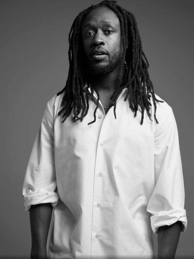 Black and white portrait of a man with long dreadlocks wearing a white button-up shirt with rolled-up sleeves.