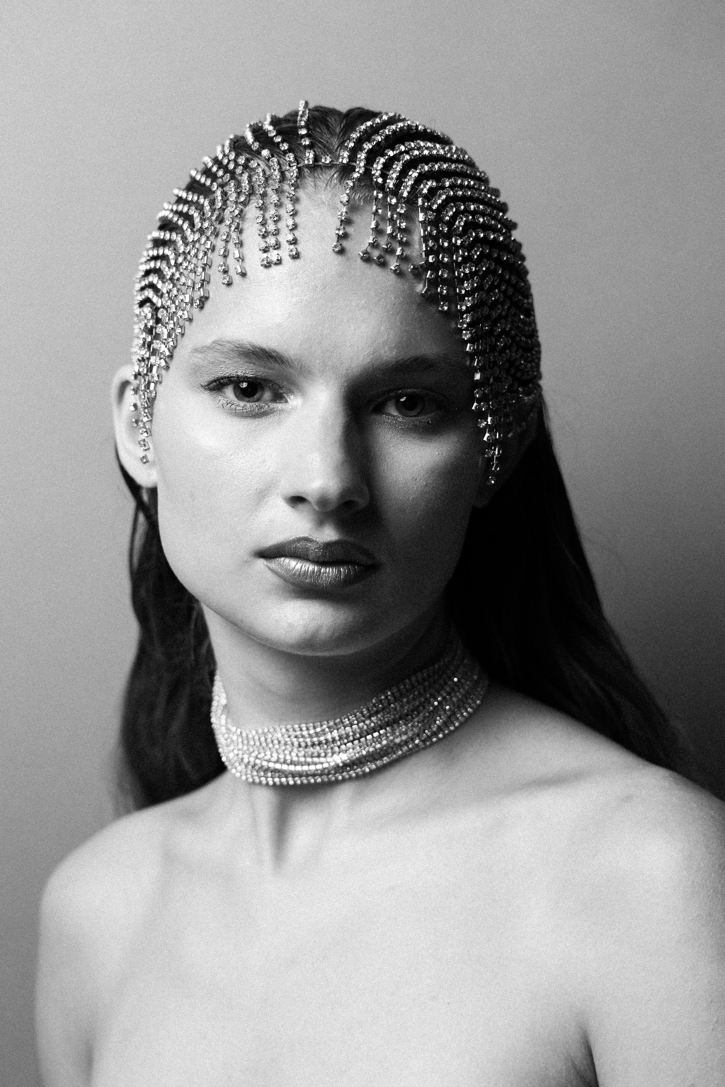 Black and white portrait of a woman with braided hair adorned with sparkling beads and wearing a multi-strand choker necklace.