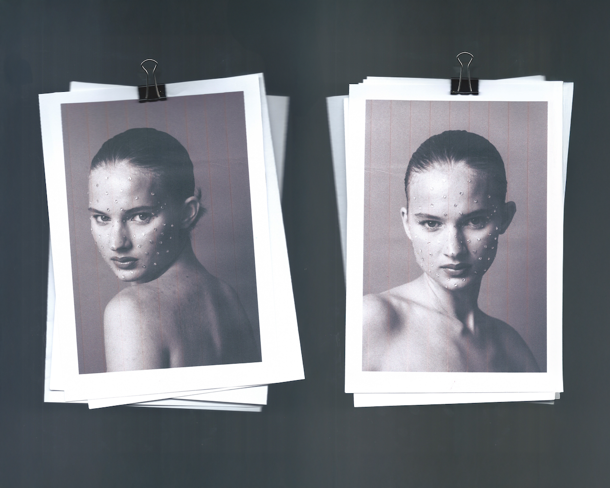 Black and white fashion photographs of a woman with slicked back hair, some with water droplets on her face, clipped to paper on a dark surface