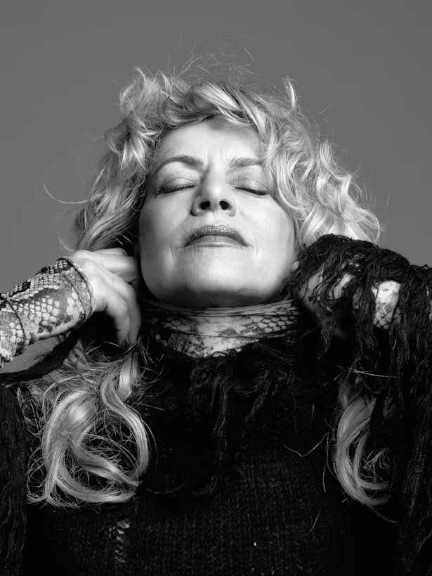 Black and white portrait of a woman with curly hair, eyes closed, touching her neck, wearing a dark, lace top.