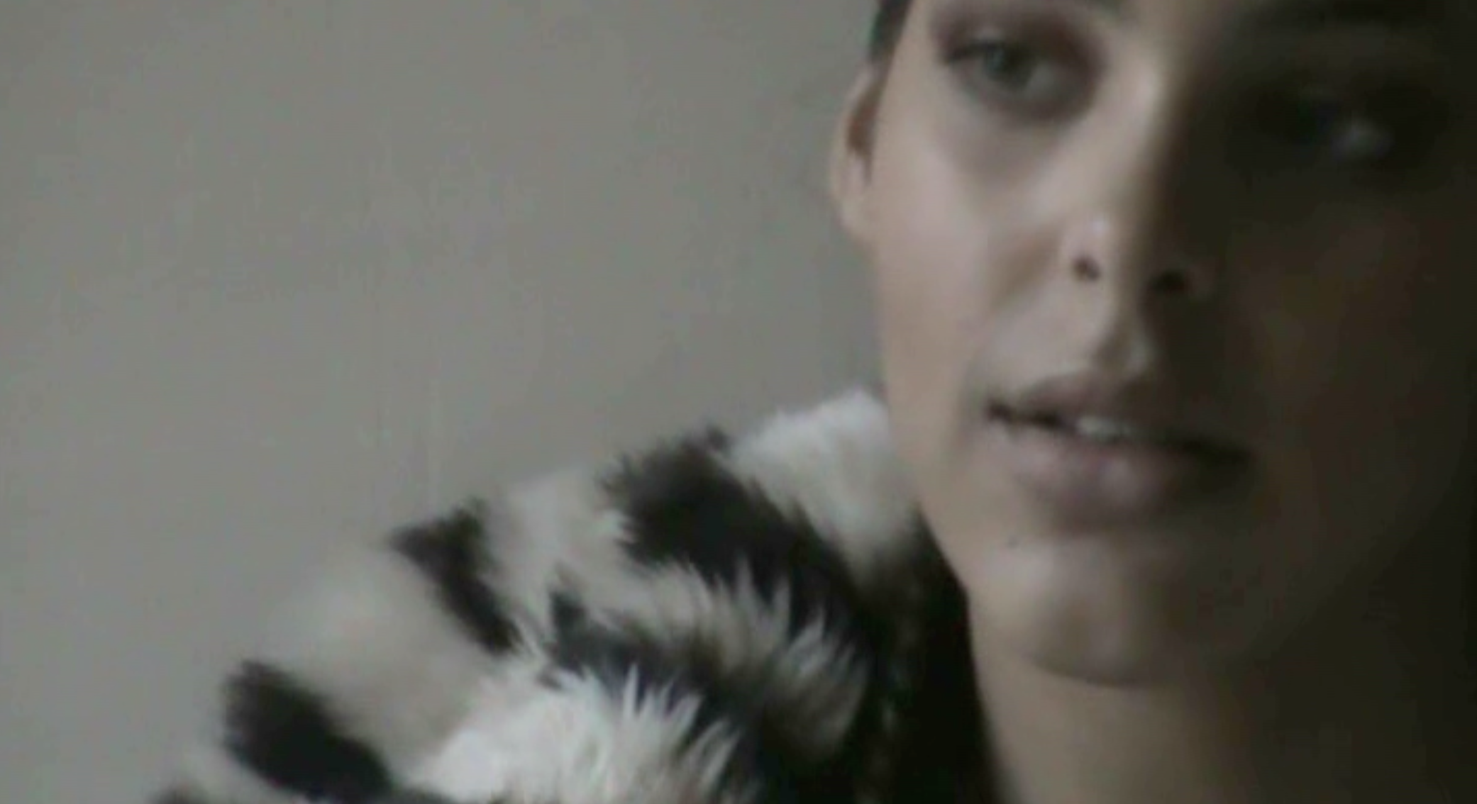 Close-up of a woman's face with light makeup, short hair, and some of her shoulder visible, wearing a black and white fur coat.
