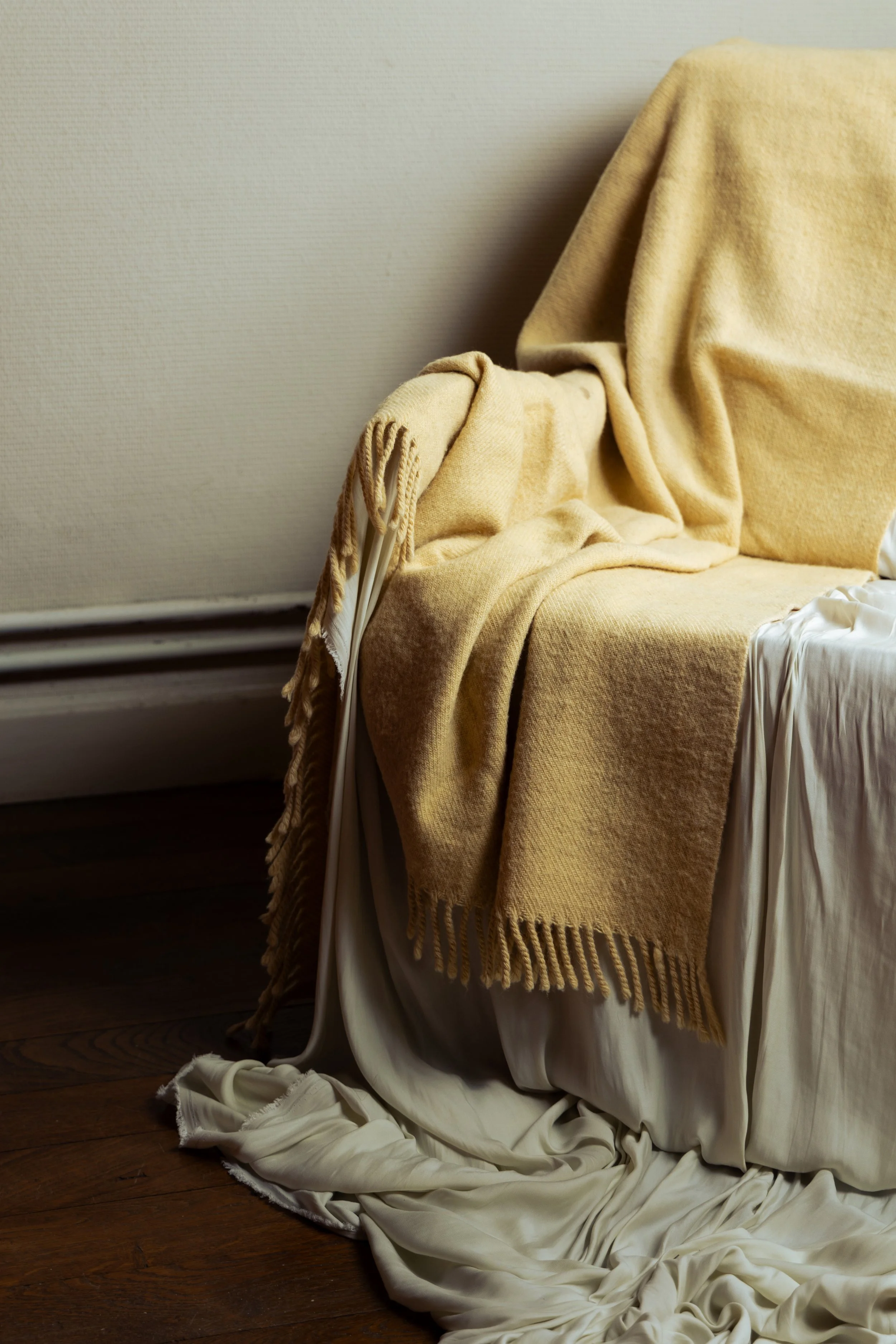 A beige blanket draped over a white chair with cream-colored fabric on a dark wooden floor.