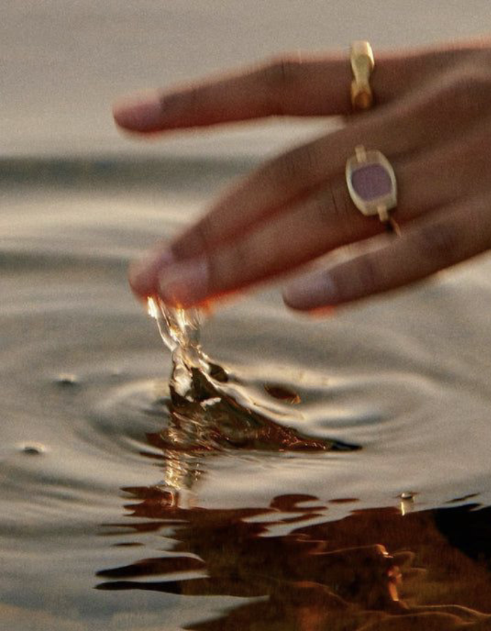 Close-up of a hand with rings, touching water surface, creating ripples and splash.