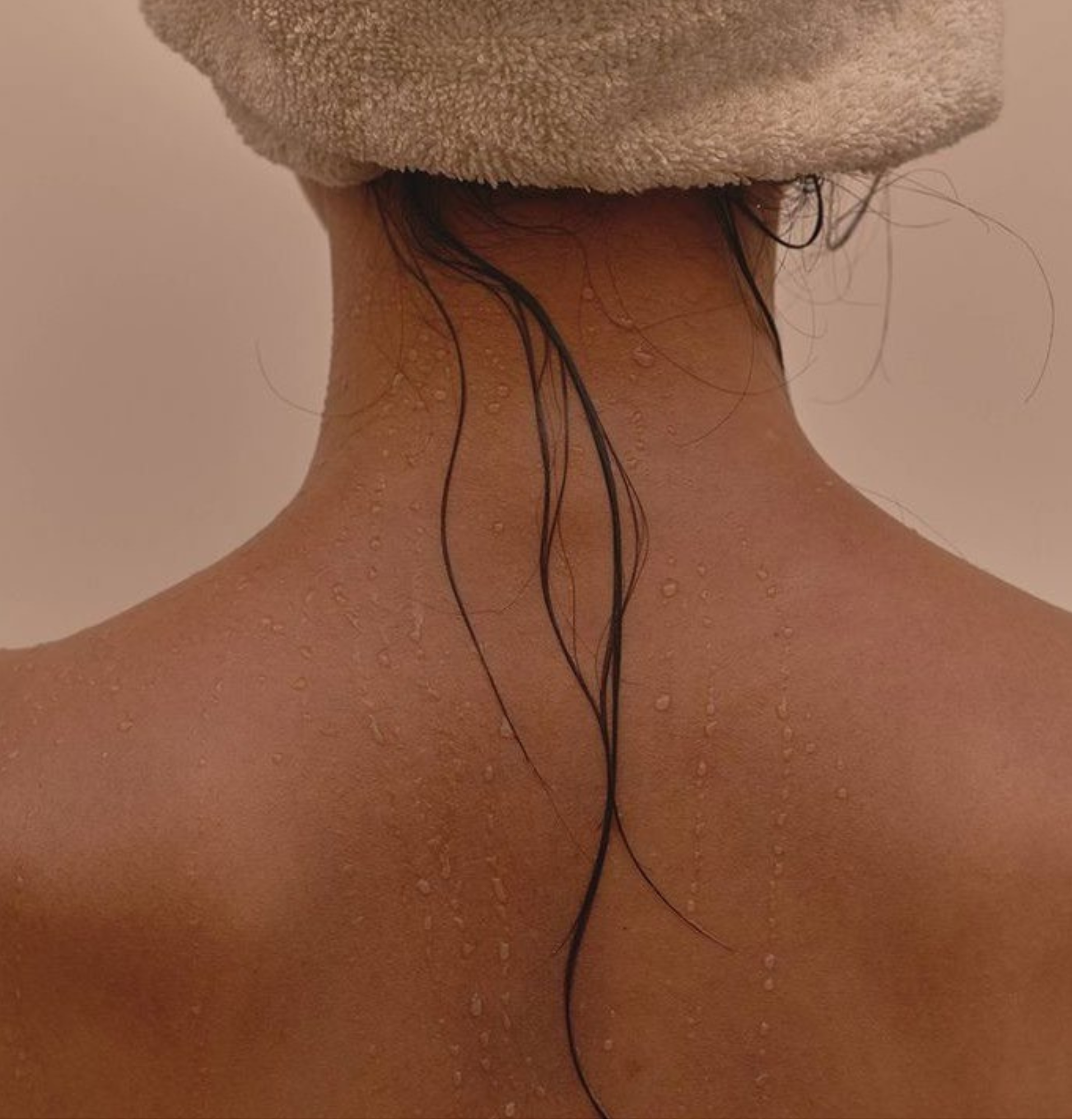 Back of a person's neck and shoulders with water droplets, wearing a towel on their head.
