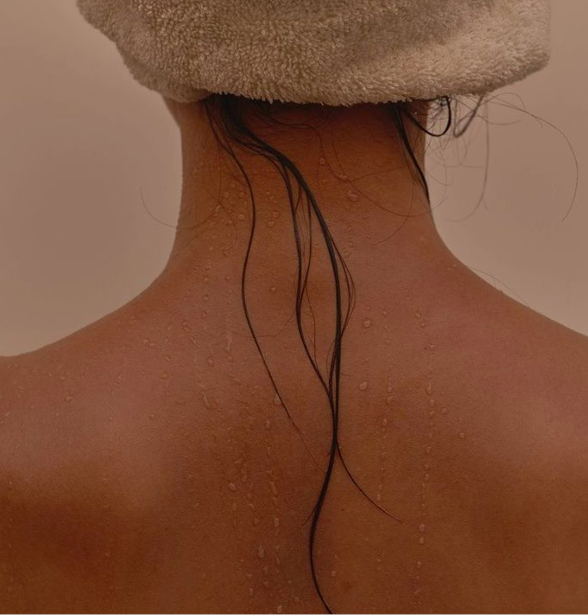 Back of a person's neck and shoulders with wet hair, water droplets, and a towel wrapped around their head.