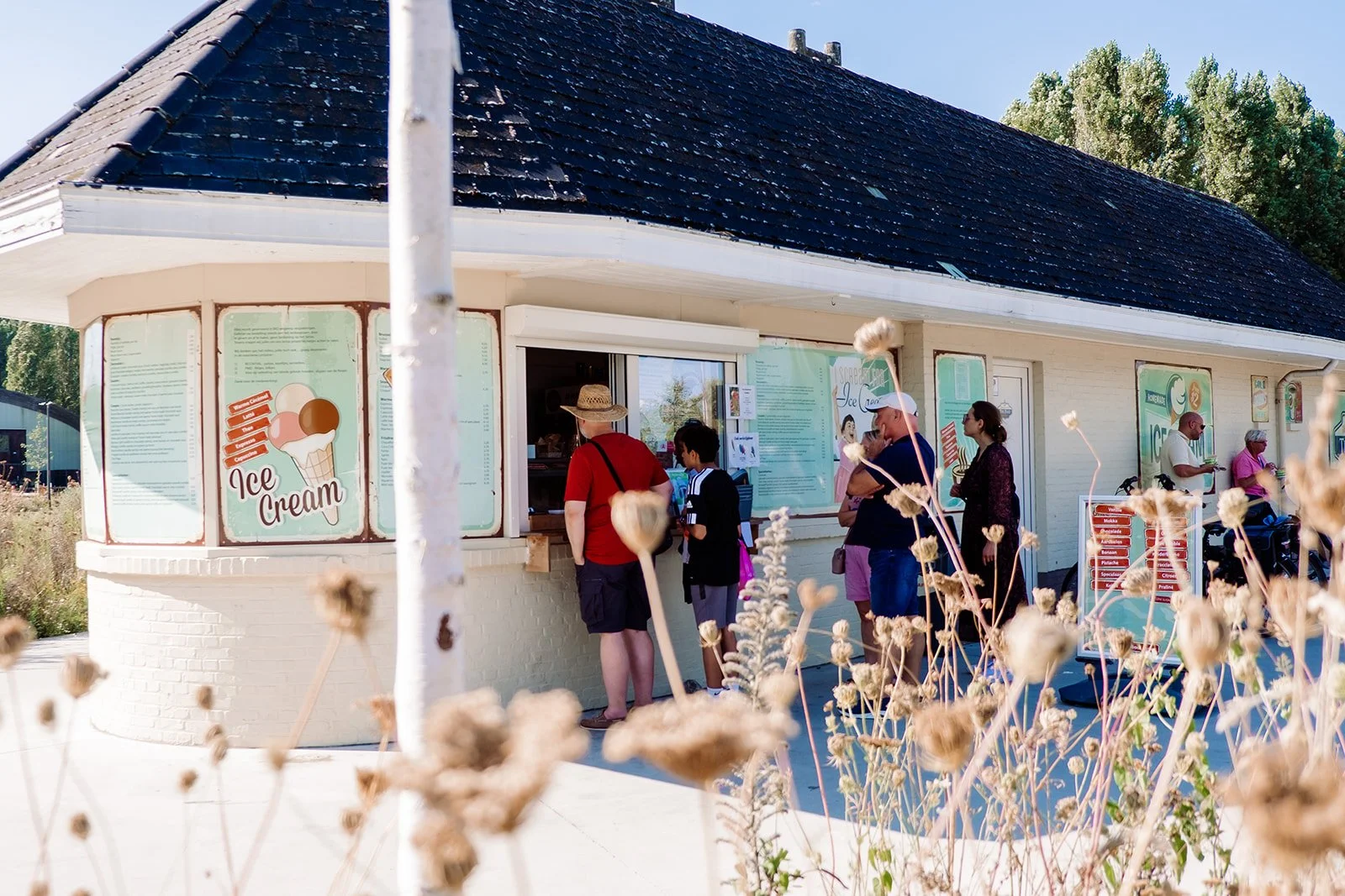 Klanten staan in de rij bij een ijswinkel op een zonnige dag.