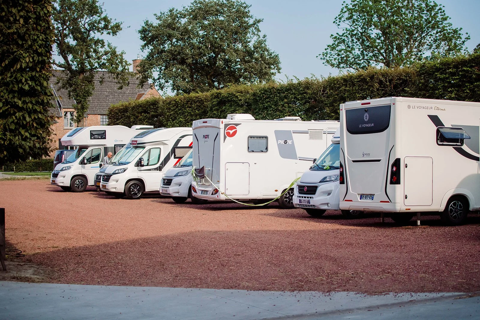 Verschillende recreatievoertuigen geparkeerd op een parkeerplaats met groene bomen op de achtergrond.
