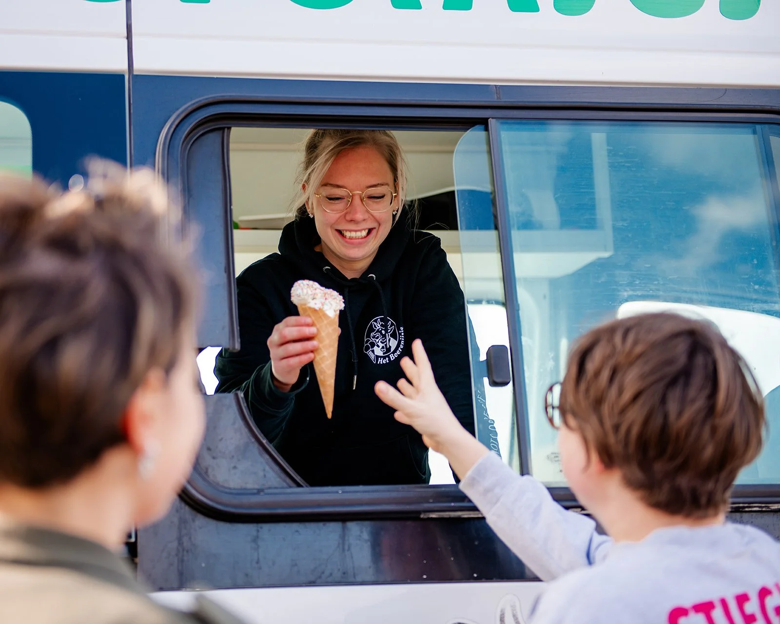 Vrouw in een ijswagen geeft ijsje aan twee kinderen die erom vragen.