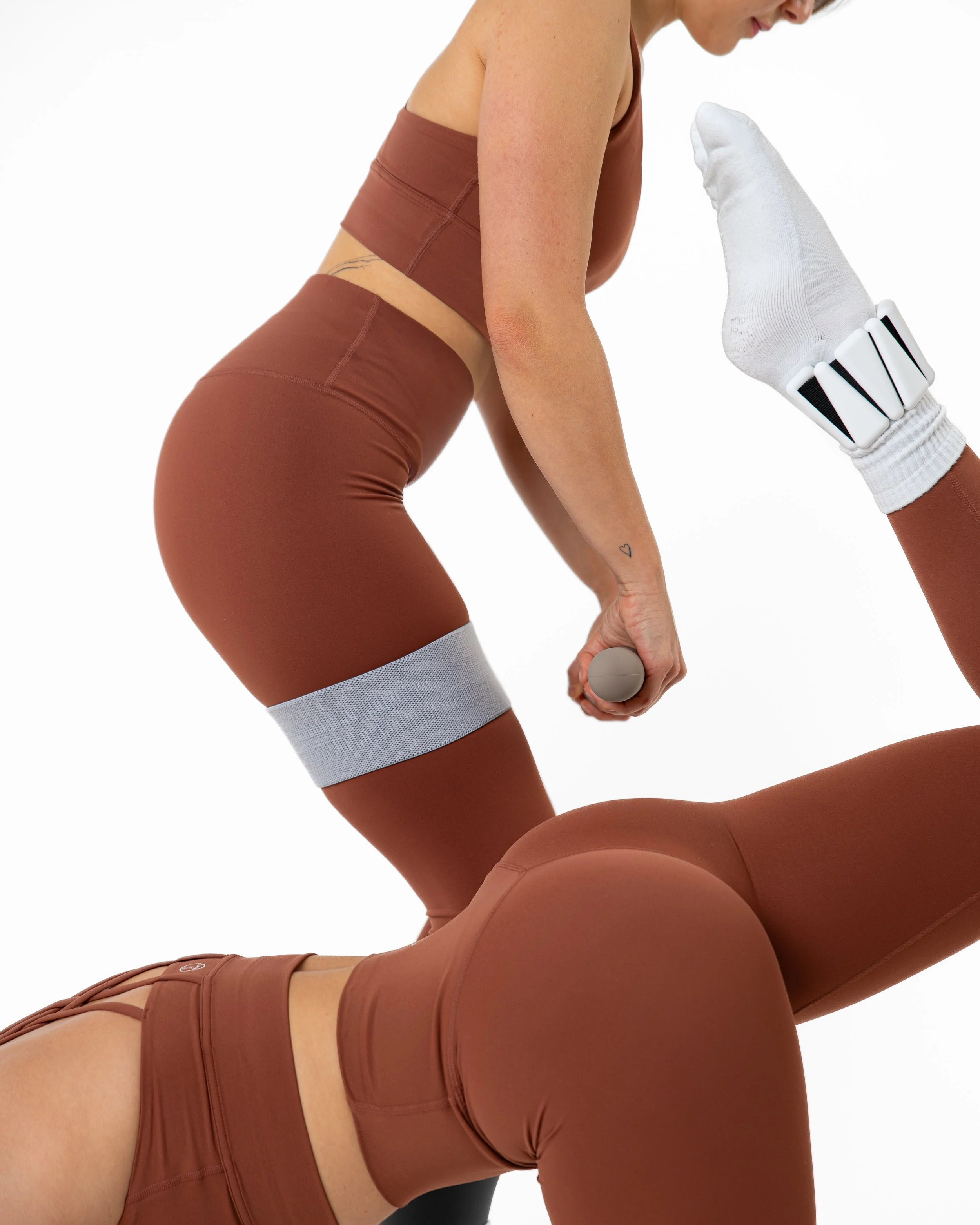 Two women in matching brown workout outfits exercising; one is holding a dumbbell, and a large hand with a white glove and a fitness tracker is pointing at her on the right side.
