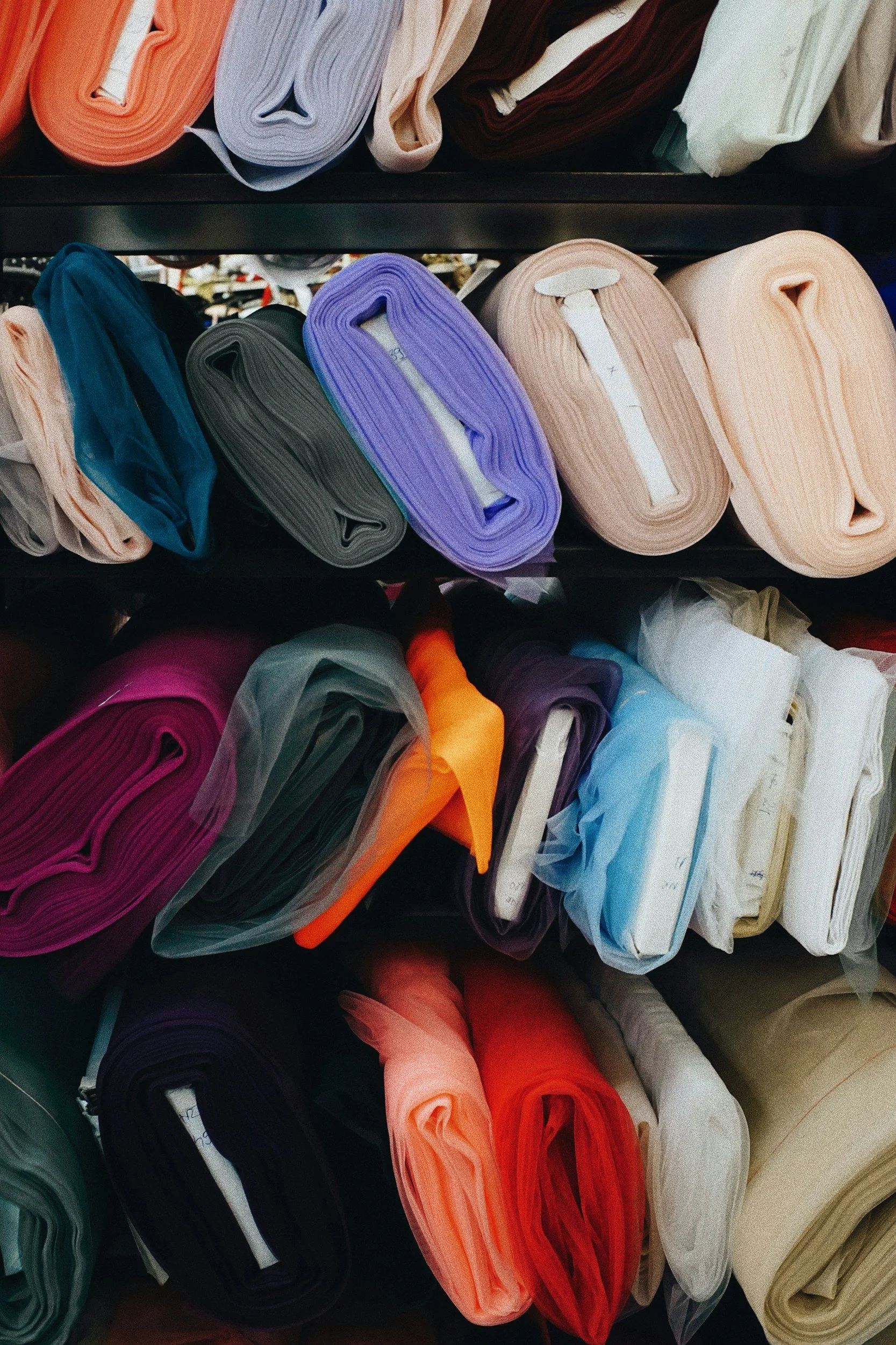 Multiple rolls of folded fabric or plastic material in various colors arranged on black shelves.