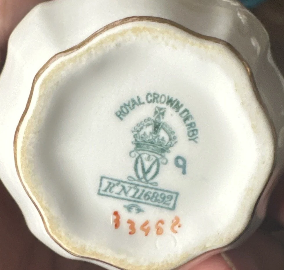The bottom of a ceramic object revealing markings, including the Royal Crown Derby logo, a crown with a shield, the number 9, and a serial number 13452 in orange.