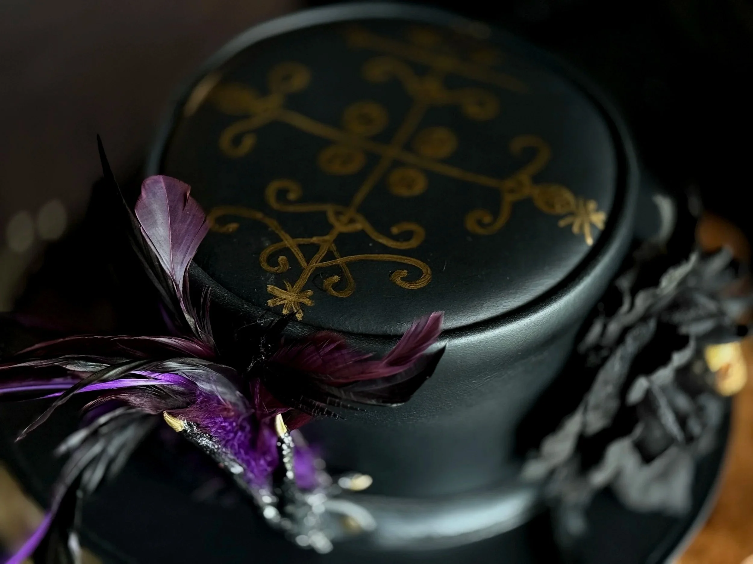 Close-up of a decorative object with intricate gold patterns on a black background, surrounded by purple and black feathers.