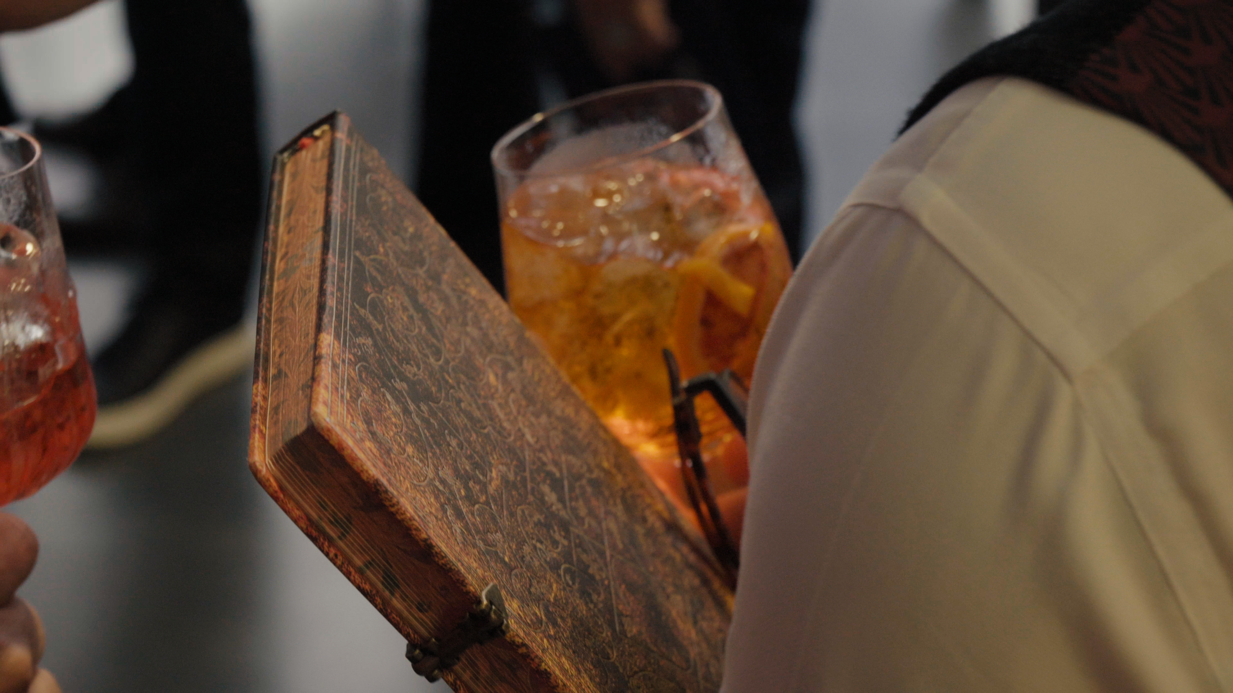 Close-up of an ornate antique book held alongside a cocktail glass, a stock footage production still for a book marketing trailer produced by Gunpowder House Productions for a UK publisher