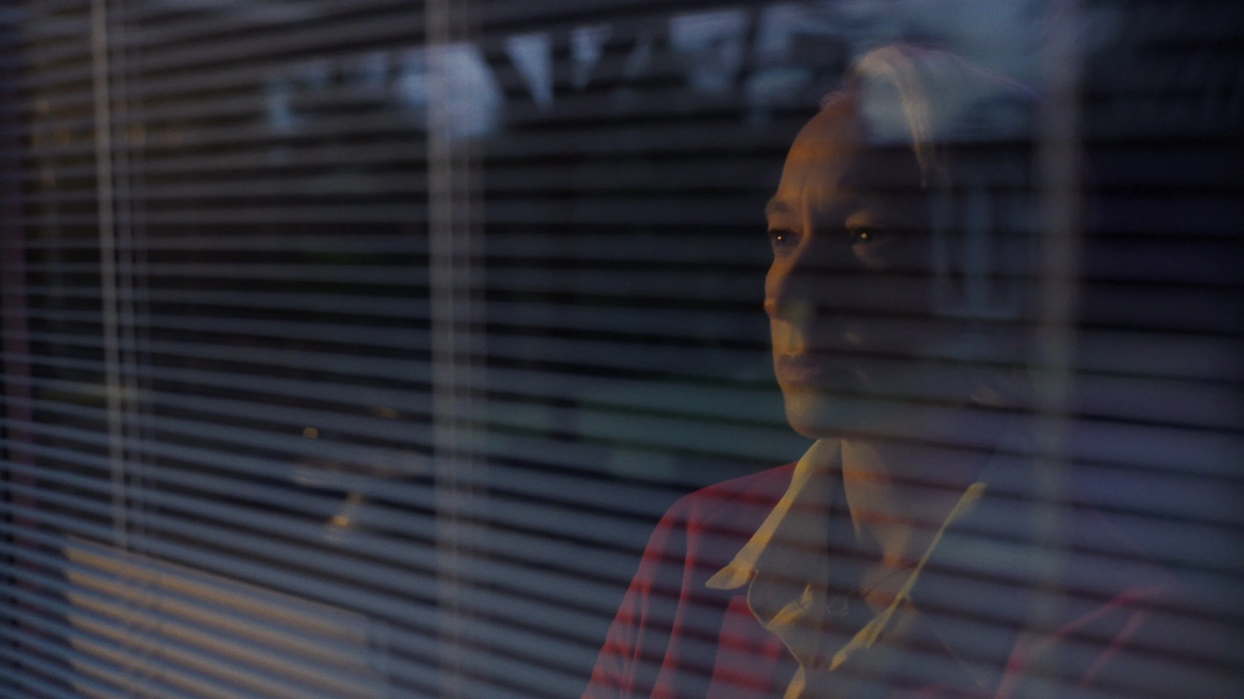 Cinematic production still of an actor seen through venetian blinds in dramatic low light, from a full cinematic book trailer produced for a UK publisher by Gunpowder House Productions