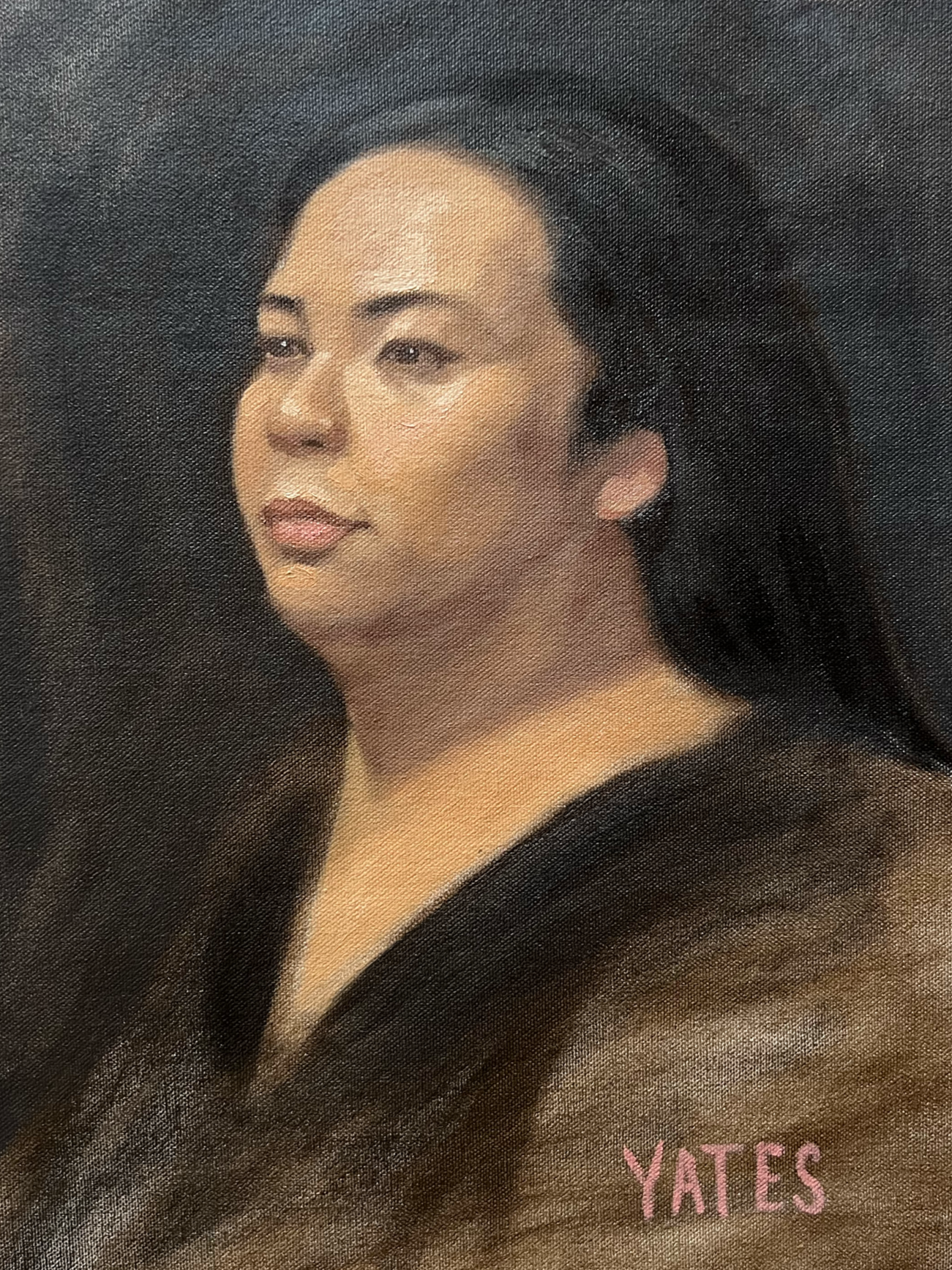 A professional portrait of a woman with long dark hair, wearing makeup, and a dark outfit. The background is black, and the word "YATES" appears in pink text at the bottom right corner.