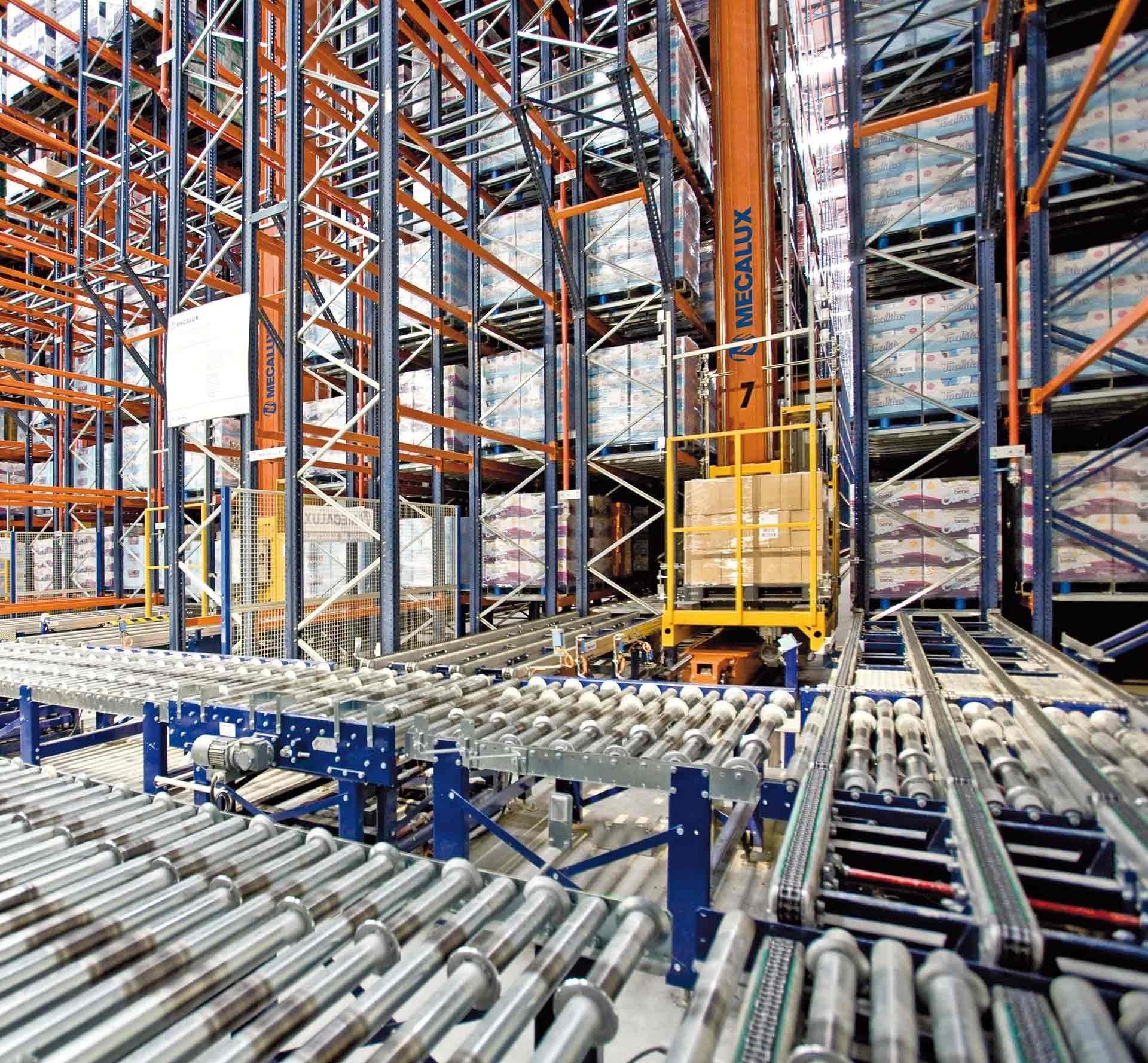 Warehouse with tall storage racks filled with boxes, a roller conveyor system in the foreground, and a yellow automated forklift moving pallets.