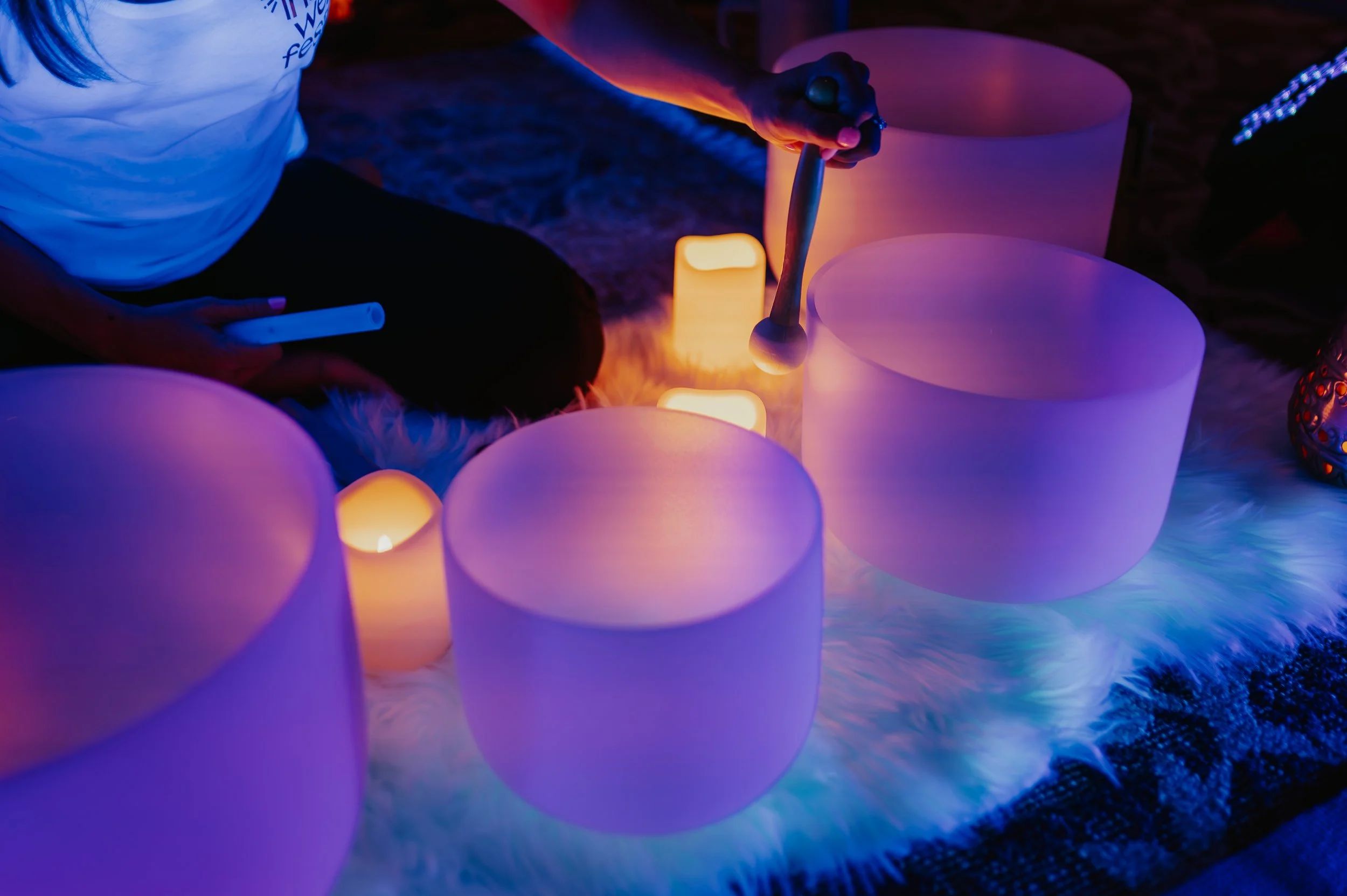 People practicing yoga in a large, illuminated, open-air architectural structure during nighttime with projected colorful sky visuals on the ceiling.