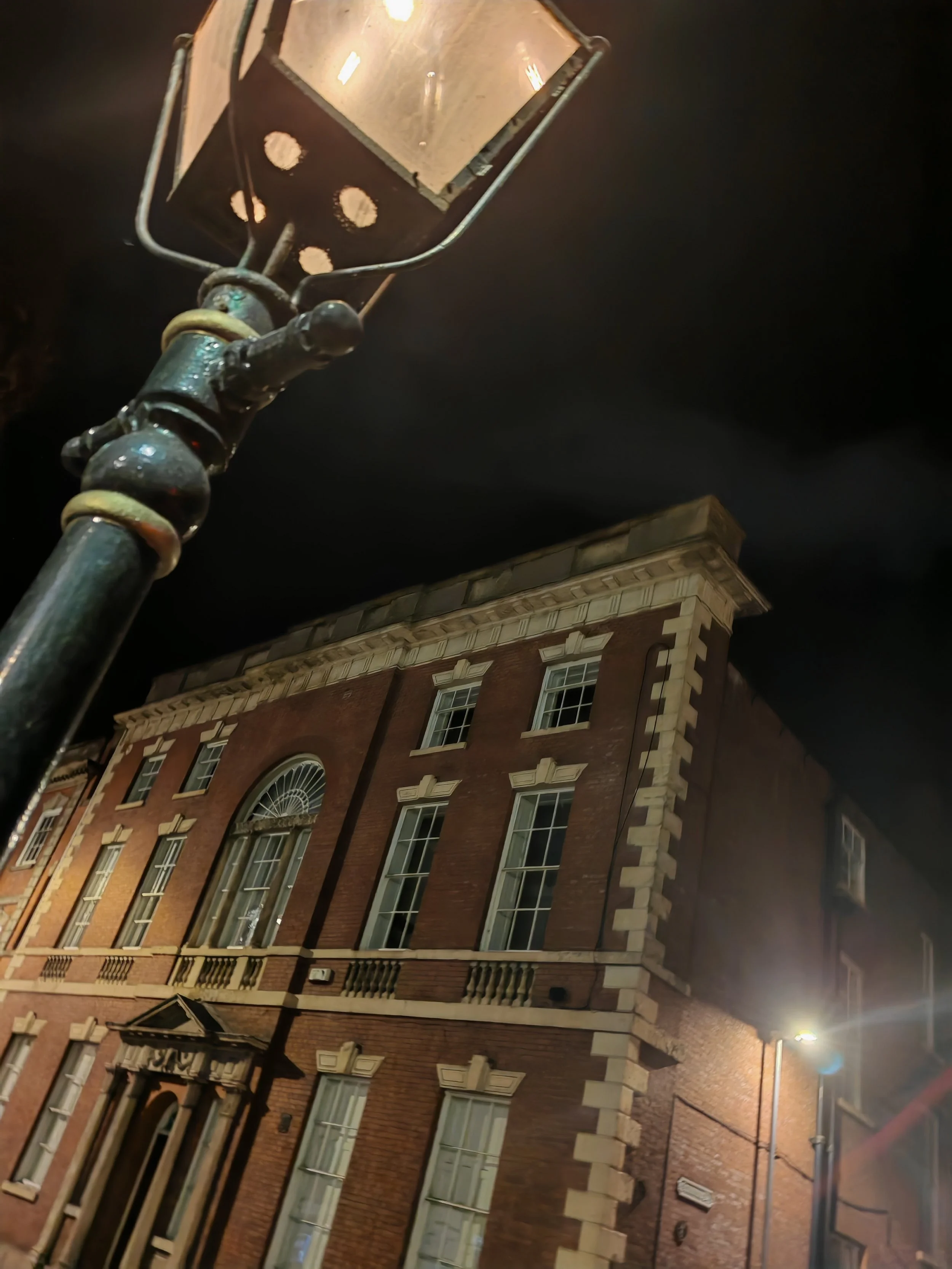 Upward nighttime view of an ornate streetlamp in front of a historic red-brick building.