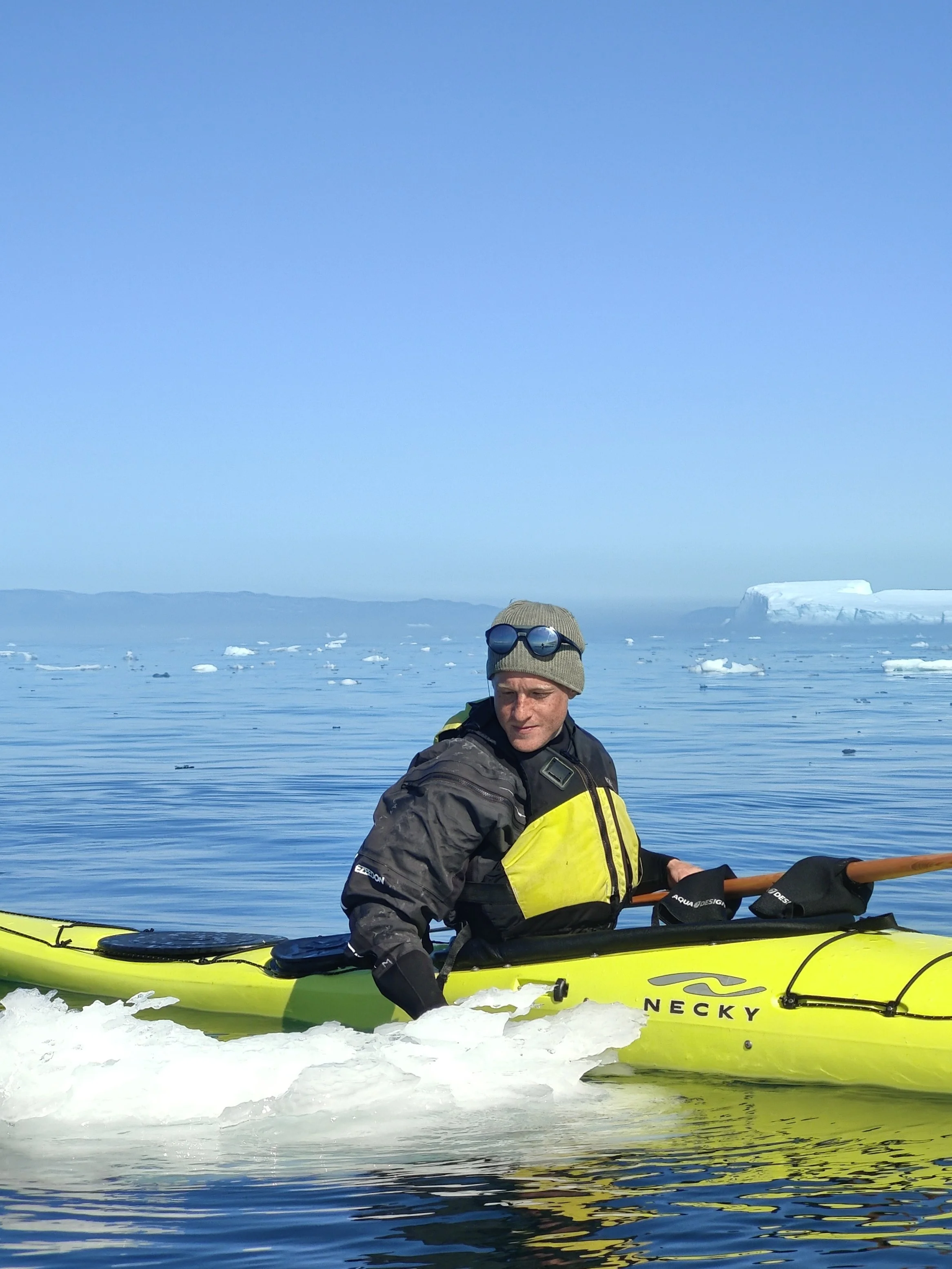 Anders Ottosen i kajak på isfyldt hav i Diskobugten under en klar blå himmel.