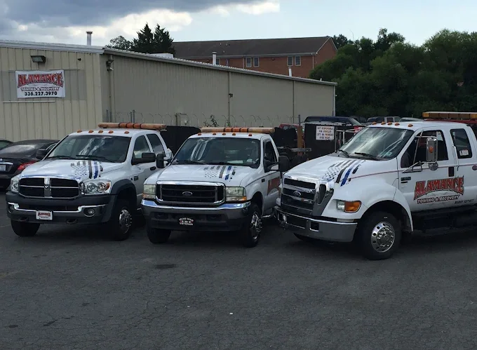 Three white utility trucks parked outside next to a building with a sign for Alarmance Security Services.