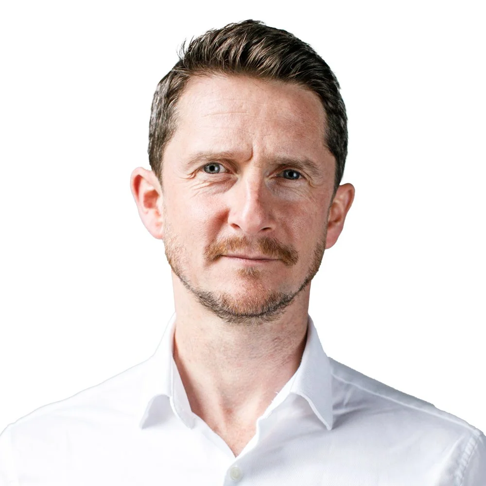 Portrait of a man with short, dark hair, light skin, and a neatly trimmed beard, wearing a white collared shirt against a plain white background.