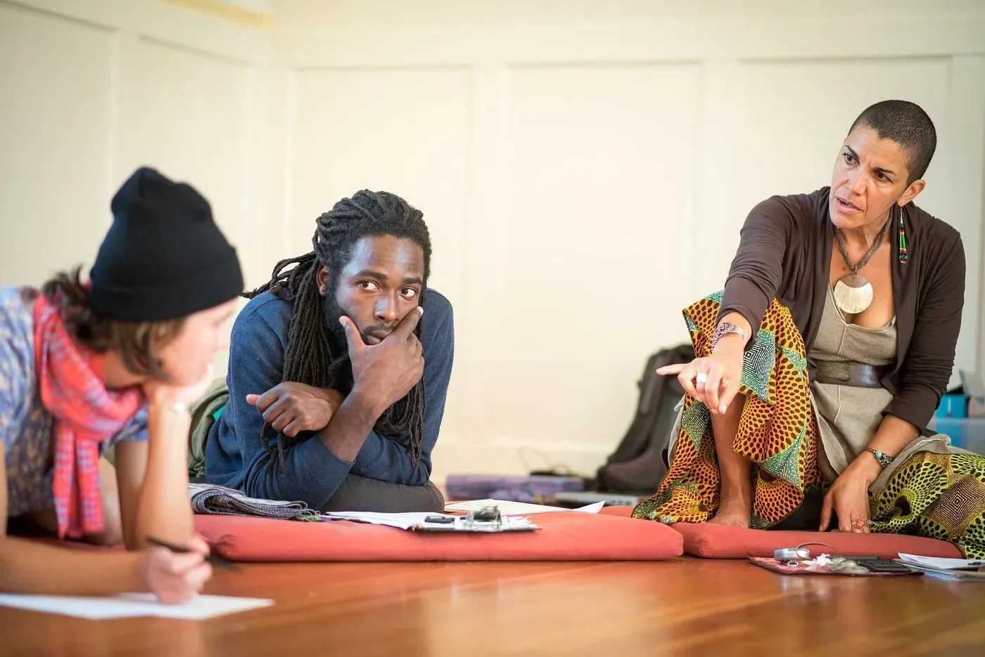Miakoda and two collaborators sit on the floor, with their clipboards and  thoughtful expressions on their face, mapping out a strategy.