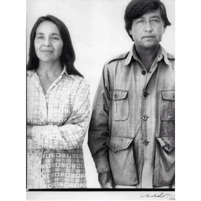A black and white image of Dolores Huerta and César Chávez, standing side by side, both with gentle stoic expressions.
