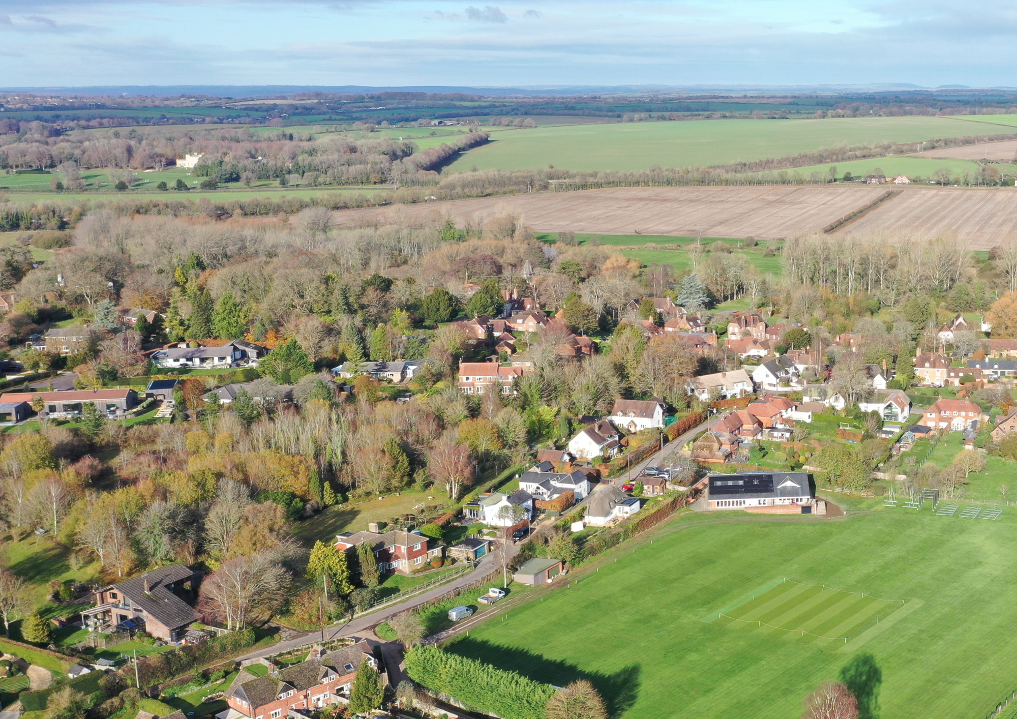 Aerial view of a small town with houses, surrounded by trees and farmland, with a green sports field in the foreground.