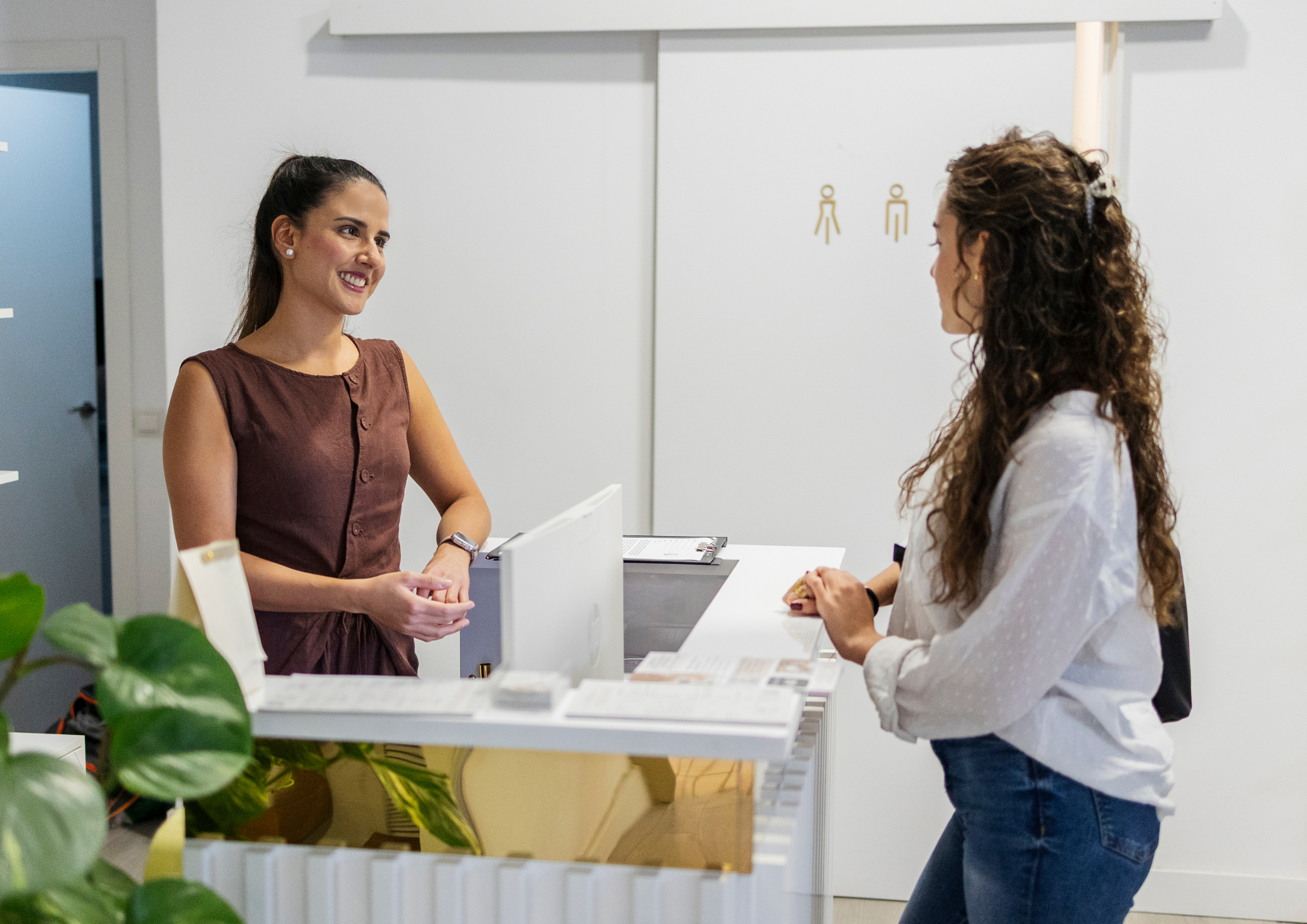 Femme souriante travaillant sur son ordinateur dans un espace lumineux et chaleureux, entourée de bois clair et de verdure, illustrant le bien-être et l’harmonie au travail.