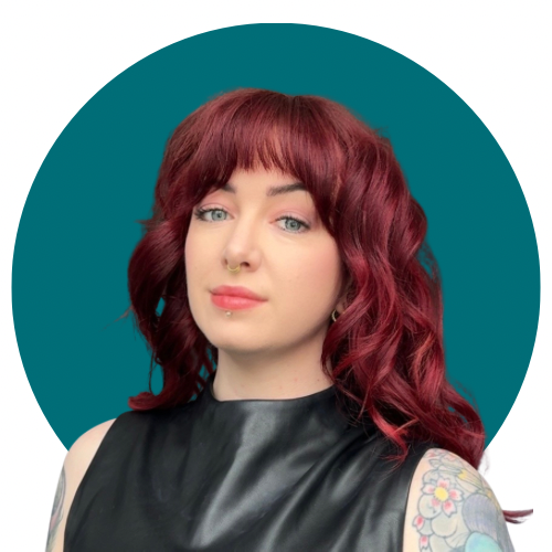 Portrait of a woman with red hair, tattoos on her arms, wearing a black sleeveless top, against a teal background.