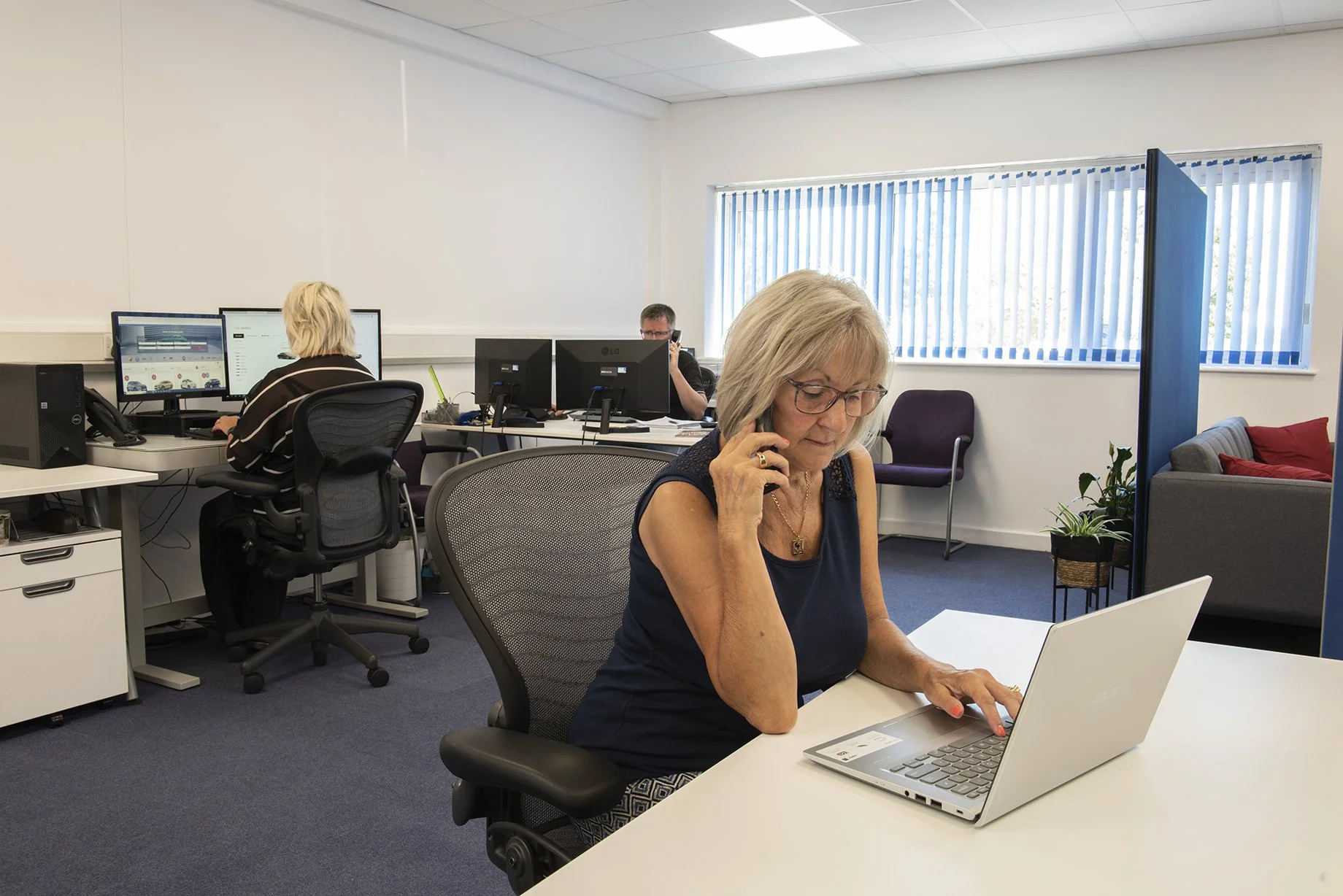 lady on the phone in an office with people working at desks around her 