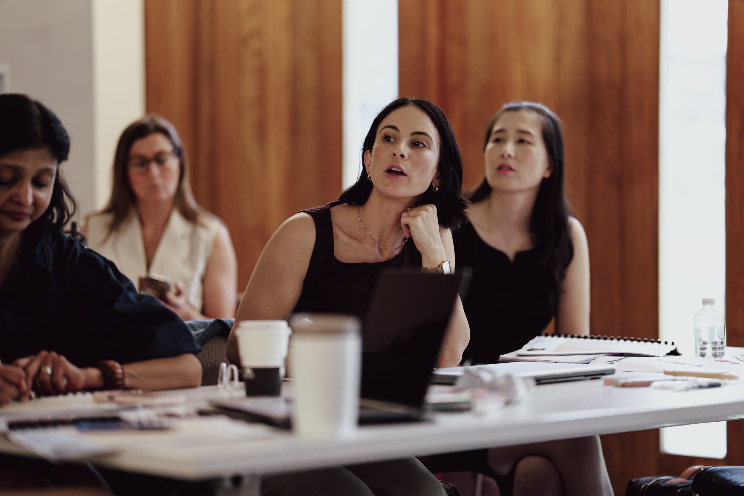 Group of women sitting at a conference table in a meeting room, engaged in discussion.