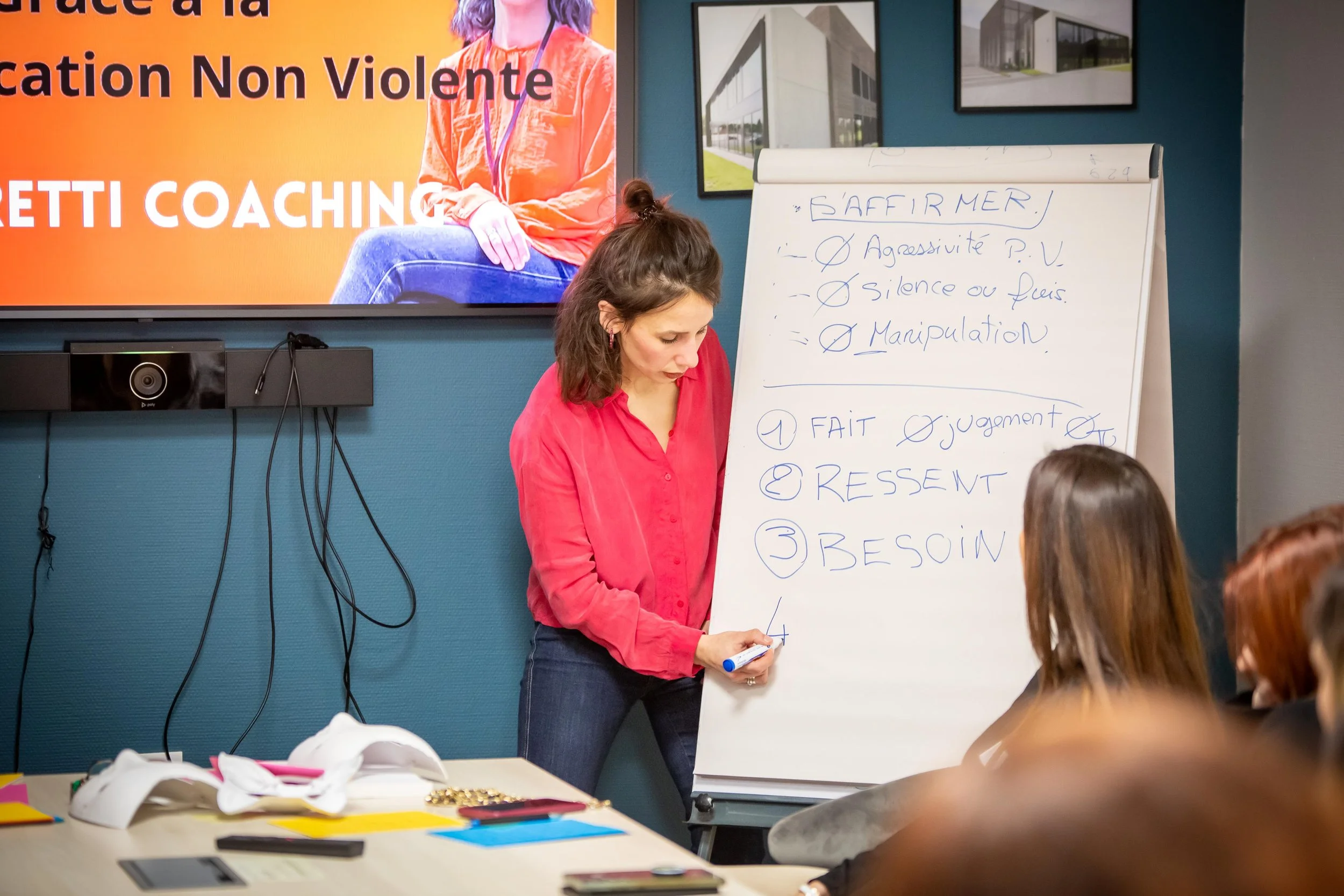Une femme donne une formation ou une présentation en français, avec un tableau blanc, dans une salle de réunion ou de formation.