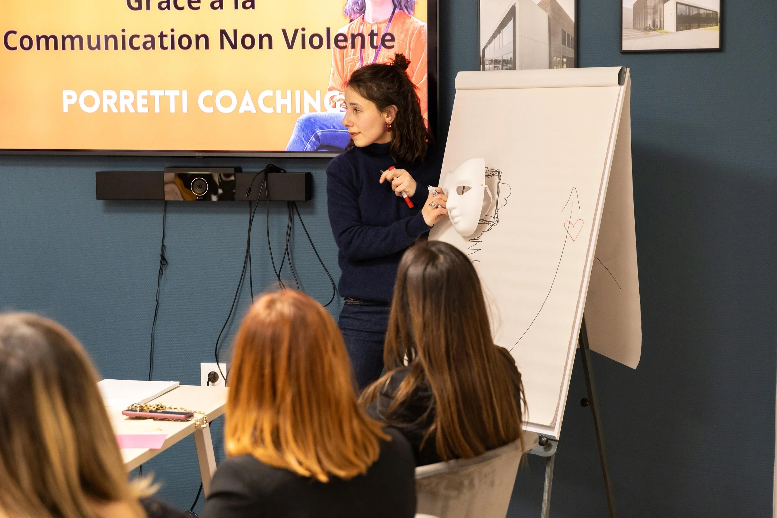 Une femme donne une présentation à un groupe de personnes, avec un tableau blanc à côté et une grande affiche à l'écran derrière elle.