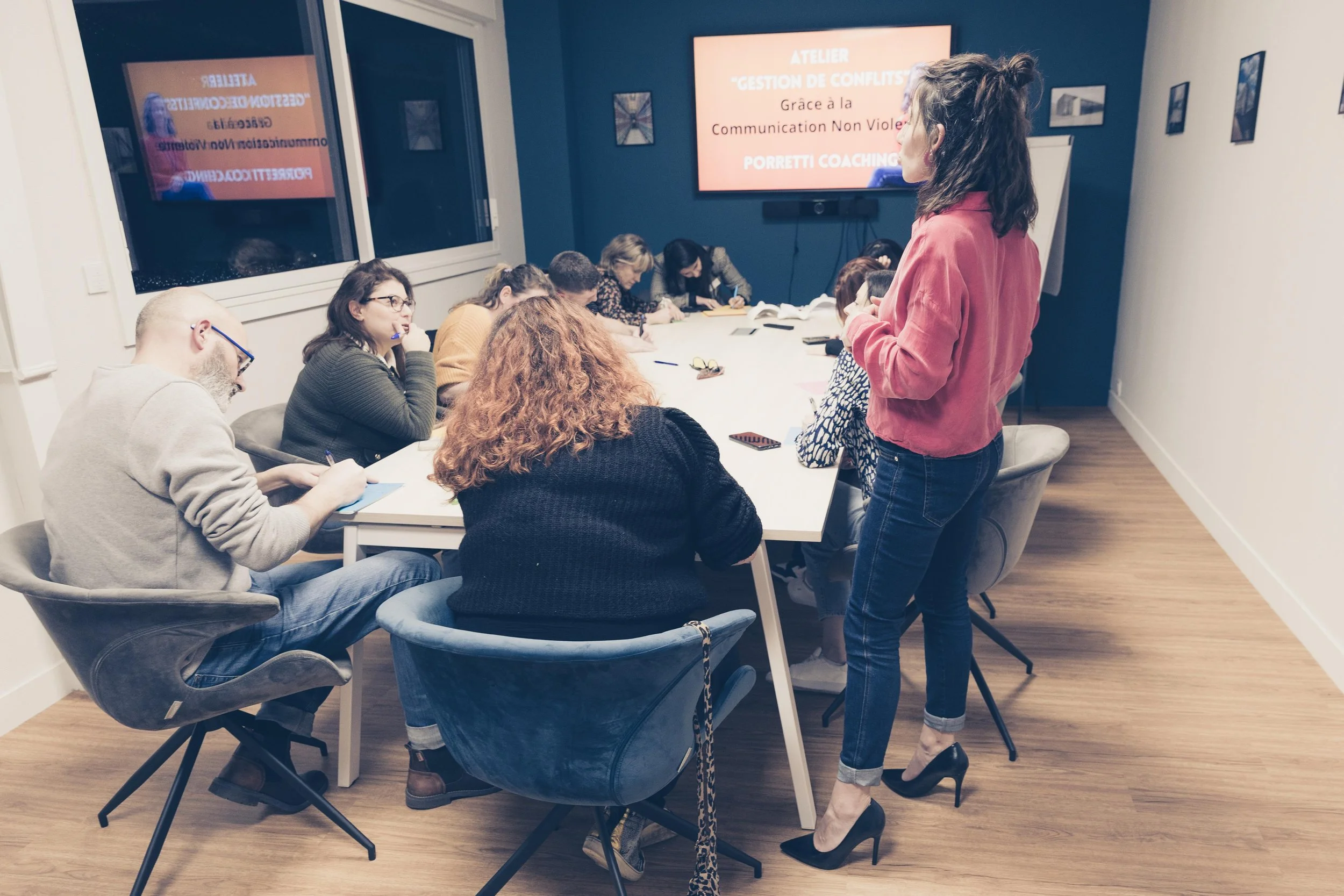 Groupe de personnes en atelier de gestion de conflits, avec une femme en train de parler et une présentation au tableau.