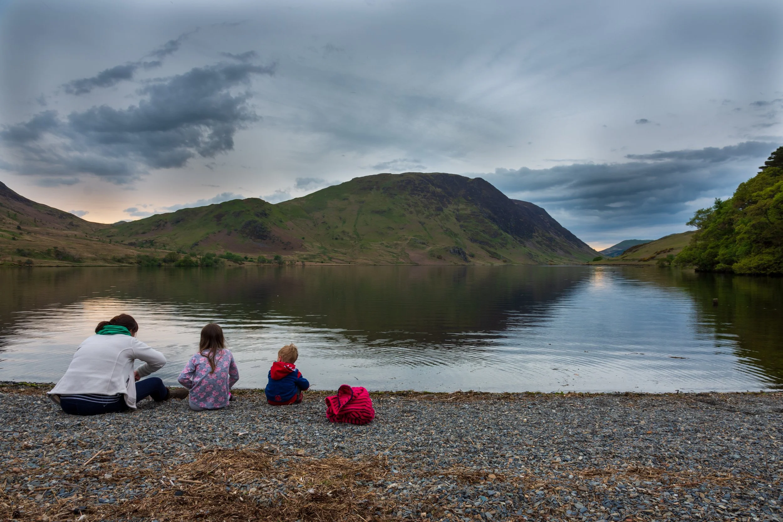 A mother and two children looking out at a calm Crummock Water near sunset in the Lake District
